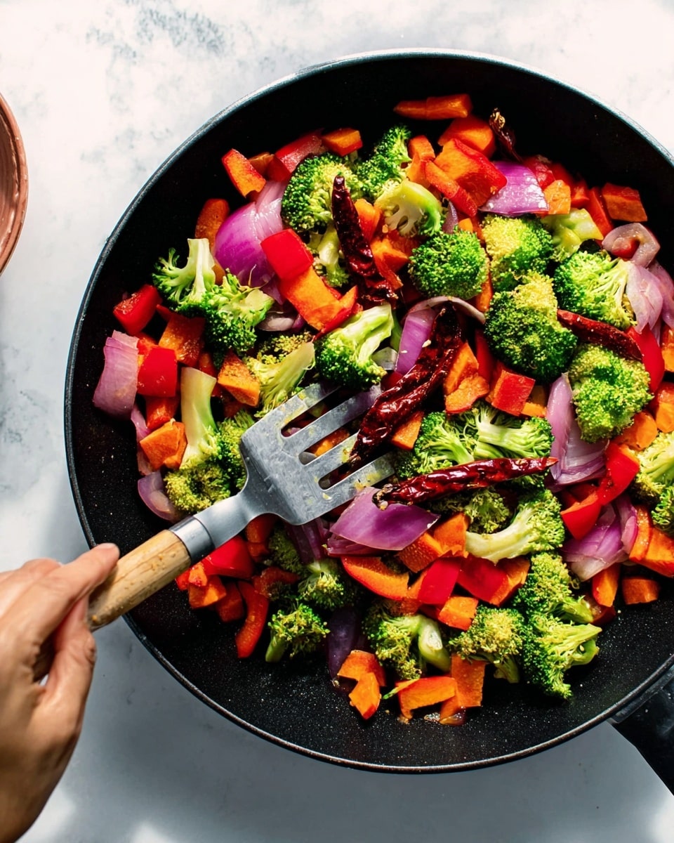 A black skillet filled with fresh chopped vegetables including bright green broccoli florets, thick red bell pepper pieces, chunky orange carrot slices, and large purple onion chunks. There are also several whole dried red chili peppers scattered throughout the mix. A woman's hand is holding a metal spatula with a wooden handle, stirring the colorful vegetables gently. The skillet sits on a white marbled surface with soft natural light casting gentle shadows. Photo taken with an iphone --ar 4:5 --v 7
