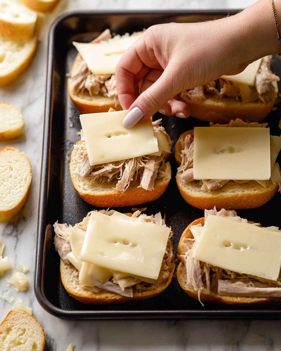 The image shows six sandwich halves on a black baking tray placed on a white marbled surface. Each sandwich is open-faced with fluffy light golden bread at the bottom, topped with shredded pale beige cooked meat. On three of the sandwiches, a woman's hand is placing or adjusting smooth, thin square slices of white cheese with small holes. Some more sandwich halves and bread pieces are visible around the tray. The scene is brightly lit and focused on the sandwiches and the woman's hand. photo taken with an iphone --ar 4:5 --v 7