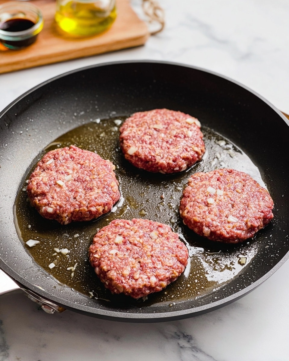 A close-up view of four raw, oval-shaped patties with visible white onion pieces mixed in, placed evenly inside a dark non-stick frying pan with a bit of oil around them. The pan is on a white marbled surface, and in the background, there are small glass containers with dark sauce and light oil on a wooden board, slightly out of focus. Photo taken with an iphone --ar 4:5 --v 7