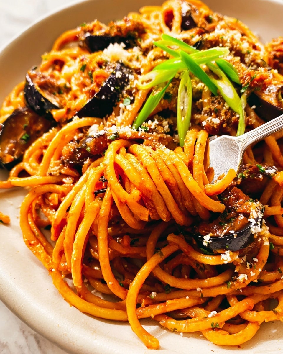 A plate with one serving of spaghetti sits in the center, with thick noodles mixed with dark brown chunks of eggplant and sauce coating the strands, topped with thin curly green onion strips and some sprinkled grated cheese. To the left is a white pan filled with more spaghetti and eggplant in sauce, with a woman's hand holding metal tongs inside the pan lifting some noodles. Below the pan is a clear glass bowl filled with water and floating sliced green onions. Above the plate is a small white bowl with grated cheese and a clear glass of water. A fork with a cream-colored handle rests on a light gray cloth to the right of the plate, all on a white marbled surface. Photo taken with an iphone --ar 4:5 --v 7