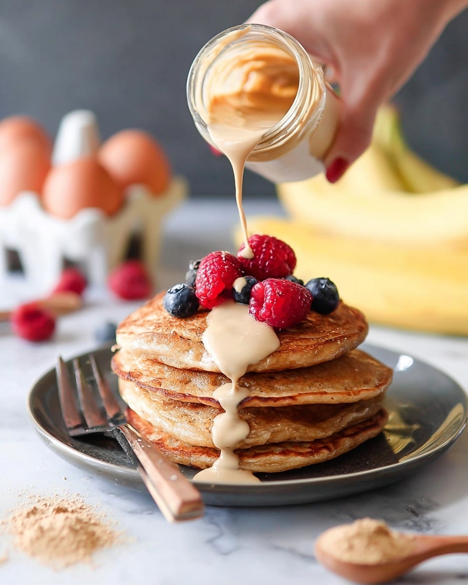 A stack of four golden-brown pancakes sits in the center of a white plate, each pancake showing slight texture and fluffy edges. On top of the stack, there are three bright red raspberries and one dark blue blueberry arranged neatly. To the left of the plate, a fork with a wooden handle rests on the white marbled surface. Surrounding the plate are scattered raspberries and blueberries. In the background, two yellow bananas lean against a white egg holder filled with eight brown eggs. On the right side of the image, a wooden-handled measuring scoop filled with a light brown powder rests on the white marbled surface. photo taken with an iphone --ar 4:5 --v 7
