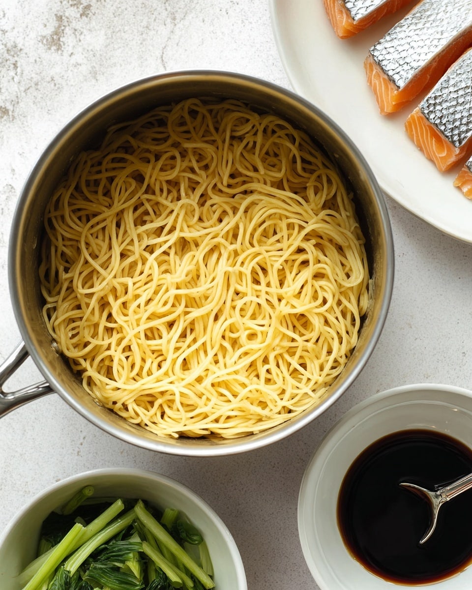 A silver pot filled with plain cooked yellow noodles sits on a white marbled surface, showing the smooth and slightly shiny texture of the noodles tangled together. Nearby, there is a white bowl filled with dark brown soy sauce, with a silver spoon resting inside. To the top right, white salmon pieces with shiny silver skins lay on a white plate, showing a clear separation of skin and flesh. At the bottom left, fresh bright green leafy vegetable pieces are placed in a white bowl, adding a fresh contrast to the scene. The overall layout shows separate raw and prepared ingredients arranged neatly, photo taken with an iphone --ar 4:5 --v 7