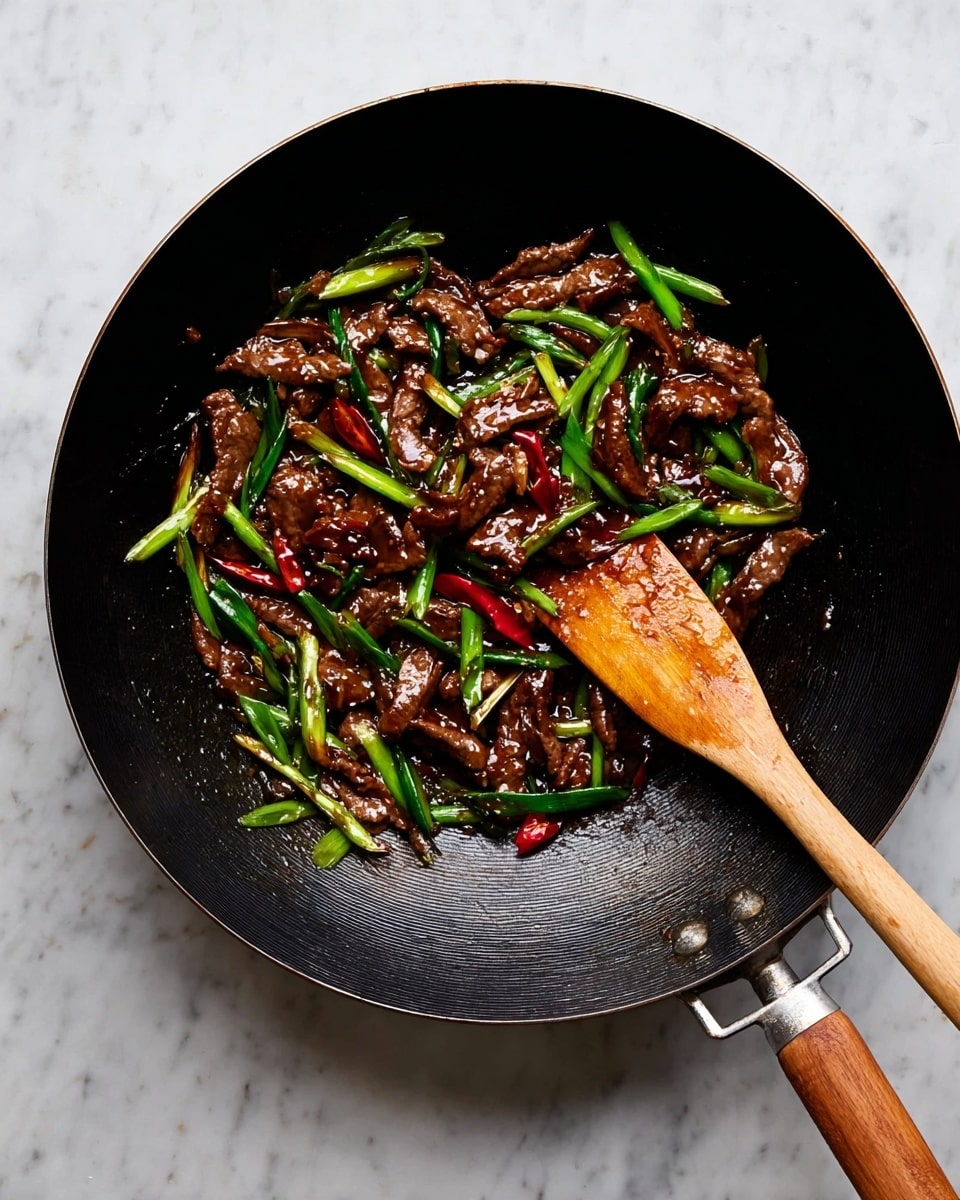 A black wok filled with a glossy, dark brown stir-fry consisting of thin strips of meat and bright green sliced scallions scattered throughout, along with a few red chili pieces adding contrast. A wooden spatula with a light wooden handle rests inside the wok, positioned on the right side. The wok has a wooden handle on the right and a metal handle on the left, placed on a white marbled surface. Photo taken with an iphone --ar 4:5 --v 7
