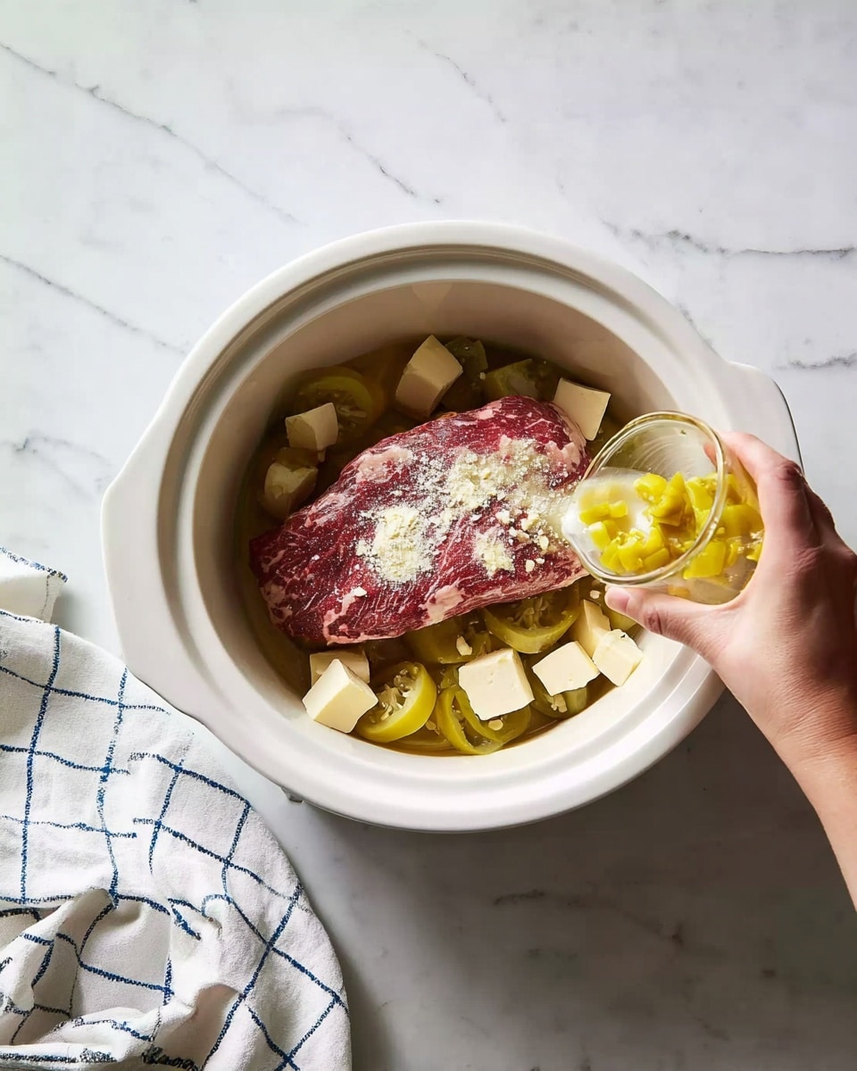 A large piece of raw red meat lies flat at the center inside a white slow cooker. On top of the meat, there are scattered small cubes of pale yellow butter and a light dusting of white flour. Around the meat in the cooker, sliced yellow-green pickled peppers are placed unevenly. A woman's hand is pouring a glass container of sliced peppers and juice onto the meat from the top right corner. Next to the cooker, a white cloth with blue grid lines rests on a white marbled surface. Photo taken with an iphone --ar 4:5 --v 7