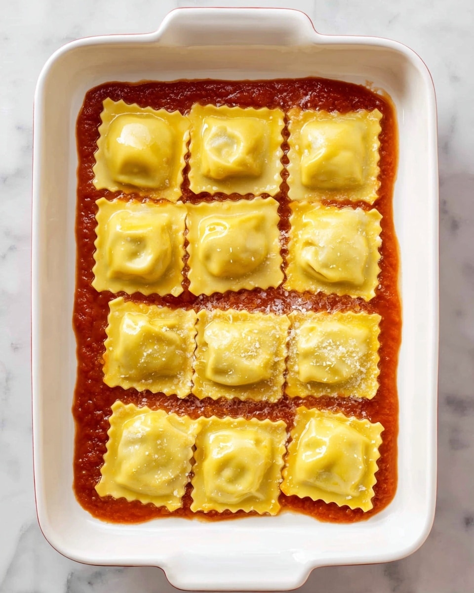 A white rectangular dish holds a single layer of 15 square yellow ravioli pieces arranged in a 3 by 5 grid, each with crinkled edges and a soft, slightly puffy texture, positioned on top of a thin layer of smooth red tomato sauce that spreads evenly across the bottom of the dish; the photo is taken on a white marbled surface. photo taken with an iphone --ar 4:5 --v 7