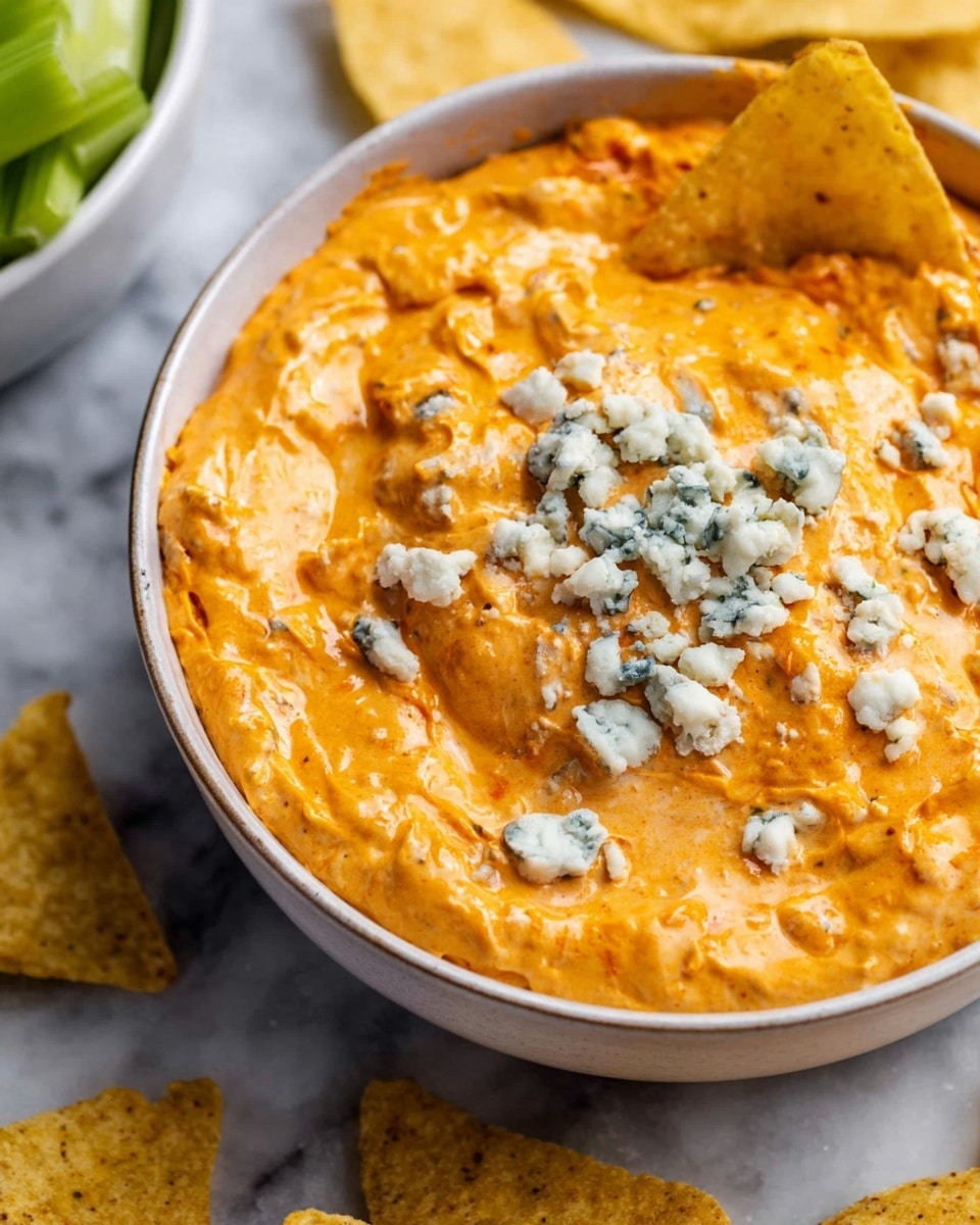 The image shows a slow cooker filled with a creamy orange dip that has a smooth and thick texture. On top of the dip, there are small crumbles of a white and blue-green cheese scattered around. A woman's hand is holding a yellow, triangular tortilla chip dipped into the creamy mixture on the right side of the slow cooker. The slow cooker is placed on a white marbled surface. photo taken with an iphone --ar 4:5 --v 7