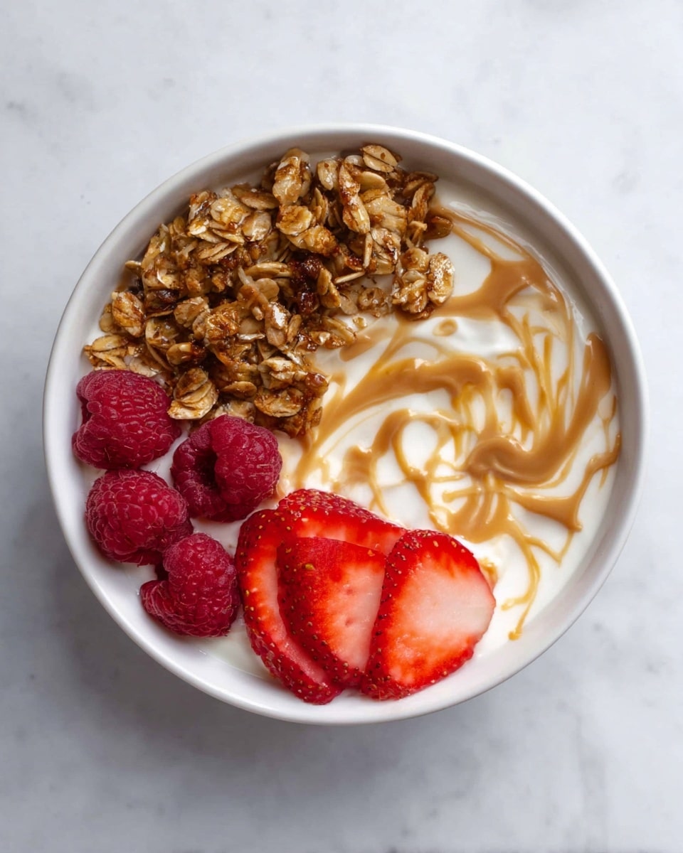 A white bowl filled with three main layers: creamy white yogurt as the base, on one side a neat pile of golden-brown granola with oats and nut pieces, in the middle a swirl of light brown peanut butter creating a marbled effect on the yogurt, and on the other side fresh red raspberries and bright red strawberry slices placed closely together. The bowl is set on a white marbled surface. photo taken with an iphone --ar 4:5 --v 7
