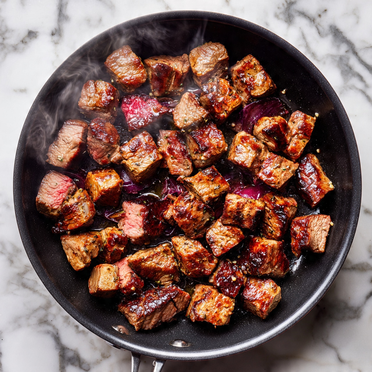 A dark round skillet filled with medium-sized browned meat cubes evenly spread across the pan, each piece showing a mix of seared dark brown and lightly cooked pink areas and emitting a light steam, all placed on a white marbled surface photo taken with an iphone --ar 4:5 --v 7