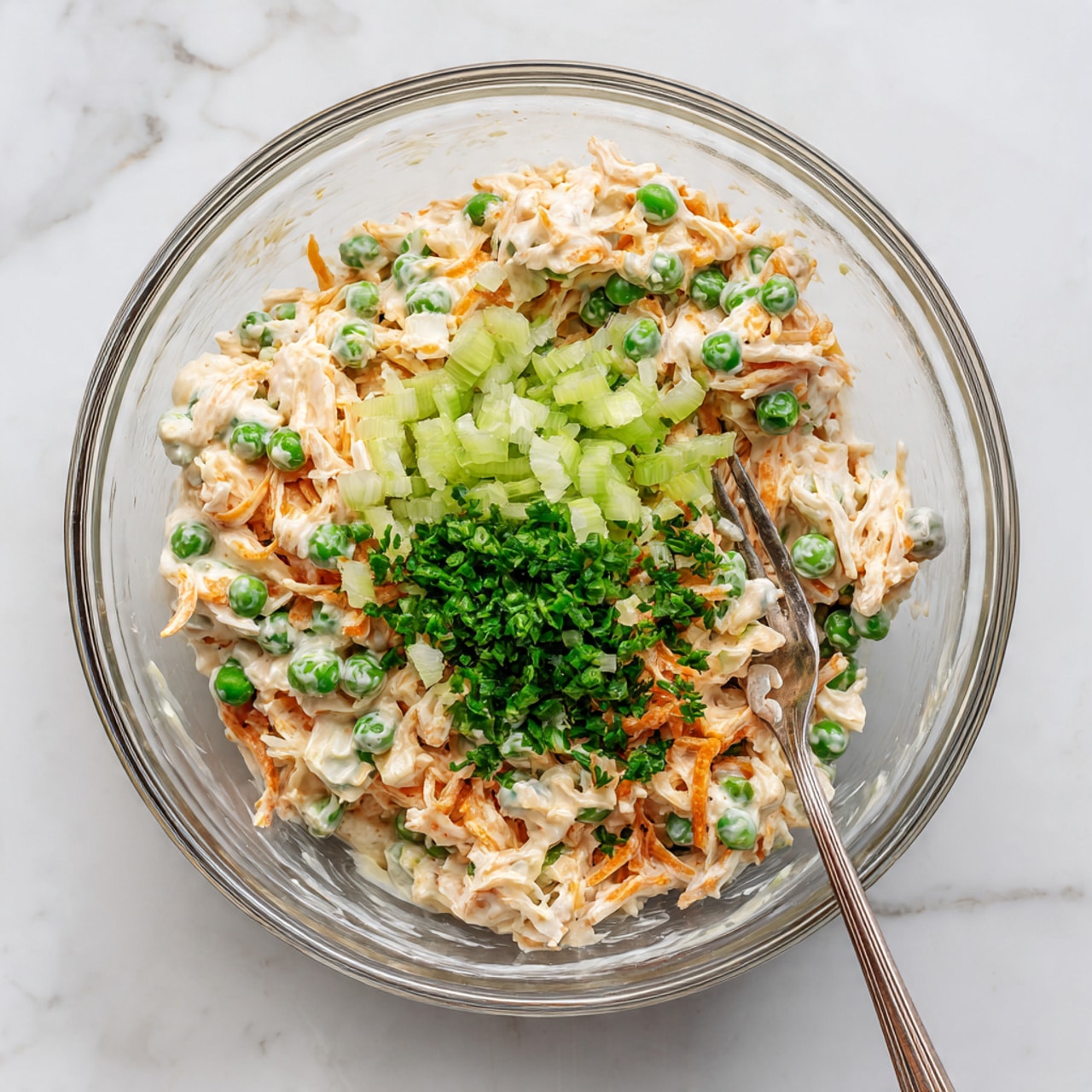 The image shows a white baking dish filled with a creamy noodle casserole. The top layer is made up of wide, soft egg noodles coated in a light beige sauce. Scattered evenly throughout the noodles are bright green peas, adding small bursts of color. The texture looks smooth and creamy with bits of finely shredded cheese and small pieces of cooked chicken mixed in. The dish sits on a white marbled surface with the casserole filling the dish completely and evenly. photo taken with an iphone --ar 4:5 --v 7