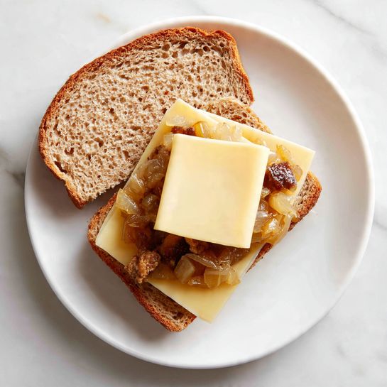 There are four grilled sandwiches with a golden-brown, crispy toasted texture, placed on a light wooden board and one on a white plate with a white marbled surface underneath. One sandwich is pulled apart slightly in the middle, revealing melted creamy white cheese stretching between the two halves. The toasted bread has a rough texture with dark brown grill marks evenly spread on the surface, showing a crunchy and appetizing look. Photo taken with an iphone --ar 4:5 --v 7