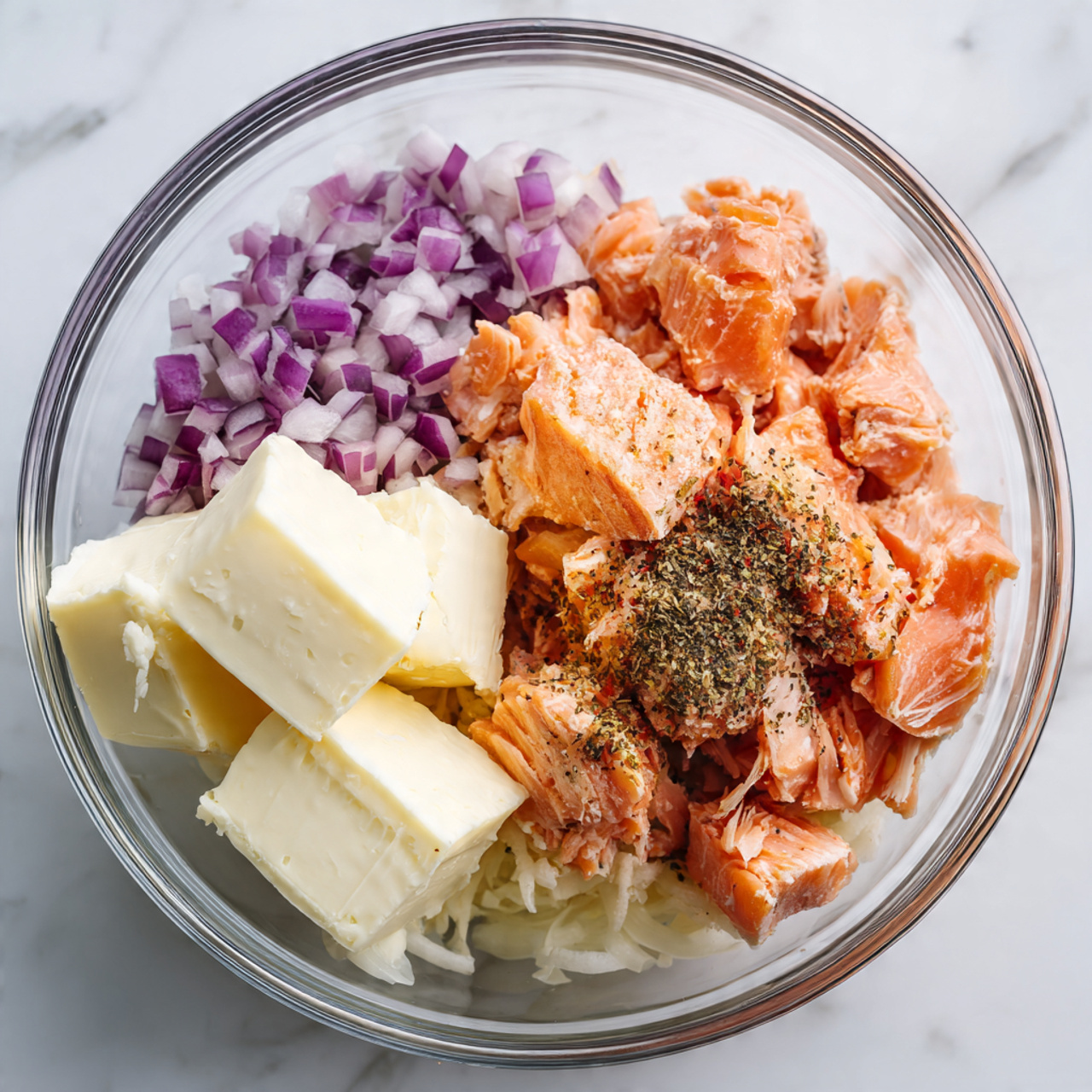 A clear glass bowl sits on a white marbled texture surface, filled with a thick, creamy mixture that is light orange with specks of darker orange and small bits throughout, giving it a chunky texture. The mixture is roughly piled in the center of the bowl, with noticeable smears of the same creamy substance spread around the sides of the bowl. Photo taken with an iphone --ar 4:5 --v 7