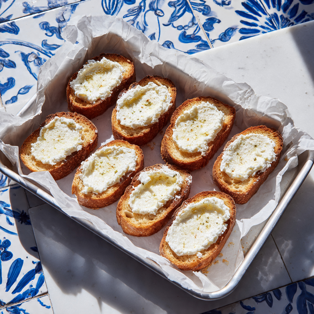 Strawberry Balsamic Bruschetta Recipe 5 The image shows about ten pieces of toasted baguette slices on white parchment paper over a white marbled plate. Each slice has three layers: a base of light golden toasted bread, a middle layer of smooth white cream cheese, and a top layer of chopped bright red strawberries. Thin green strips of fresh basil are sprinkled on top of the strawberries, and there are dark brown balsamic glaze drizzles over the strawberry layer and the plate. A whole strawberry sits on the plate, and a few small green basil pieces are scattered around. The background is a white marbled surface with small green basil leaves. photo taken with an iphone --ar 4:5 --v 7