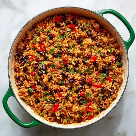 A large white pot with green handles sits on a white marbled surface, filled with a cooked rice dish mixed evenly with small black beans, browned ground meat, and diced red bell peppers. The rice is golden-brown and moist, with a soft texture, and the beans and meat are scattered throughout, giving the dish a hearty look. The edges of the pot show some sauce stains, hinting at the rich flavors inside photo taken with an iphone --ar 4:5 --v 7