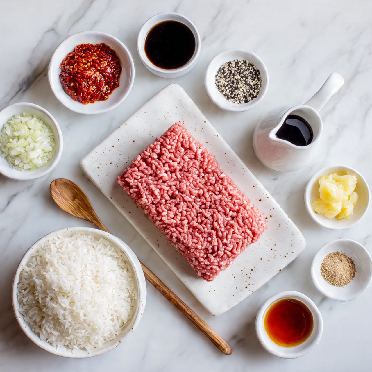 A flat rectangular block of raw pink ground meat sits on a large white plate with small brown speckles, centered on the right side of the image; to its lower right is a white bowl filled with cooked white rice, with a light brown wooden spoon resting inside. Surrounding the meat and rice on a white marbled surface are small white bowls each holding different ingredients: finely chopped white onions at the top center, black pepper next to it on the right, dark soy sauce in a small white jug below the pepper; on the left side of the meat is a small bowl of red chili sauce at the top, crushed red pepper flakes below it, a small bowl with light yellow finely minced garlic next, then another small bowl containing minced ginger below, a small dish with a dark reddish liquid further down, and finally a bowl of light brown powdered seasoning near the bottom center. Photo taken with an iphone --ar 4:5 --v 7