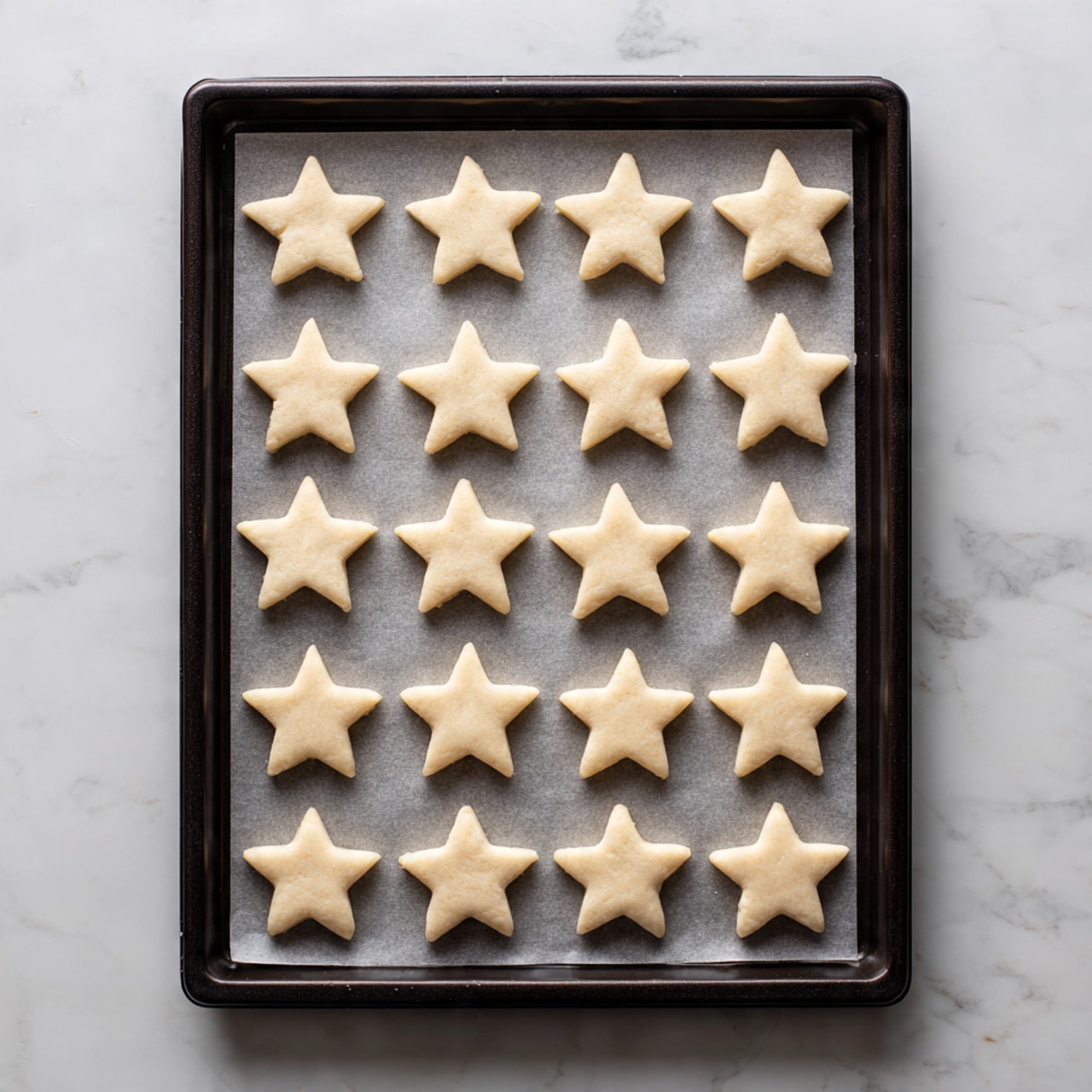 A woman's hand holds a small star-shaped cookie being dipped into a clear glass bowl filled with a cinnamon and sugar mixture, showing the cookie covered in a light brown powder. Nearby on the left, there is a cooling rack holding two neat rows of plain star-shaped cookies that are light golden brown with slightly darker edges. Above the cookies is another clear glass bowl containing melted yellow butter with a green silicone brush resting on the cooling rack next to it. The whole scene is set on a white marbled surface. photo taken with an iphone --ar 4:5 --v 7
