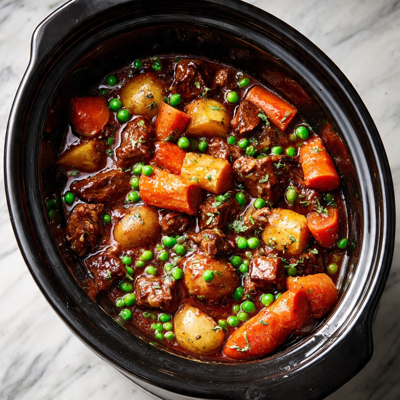 A white bowl filled with a thick stew showing chunks of dark brown beef, small bright green peas, orange carrot slices, and light tan potato pieces in rich brown gravy, garnished with small green herb leaves. A toasted slice of light golden brown bread rests on the side edge of the bowl. A silver spoon is partially submerged in the stew inside the bowl. In the top background, another white bowl with the same stew is partially visible, alongside another toasted bread slice on a white wooden plate. The setting sits on a white marbled surface with scattered green herbs and a gray textured cloth visible on the lower right side. Photo taken with an iphone --ar 4:5 --v 7
