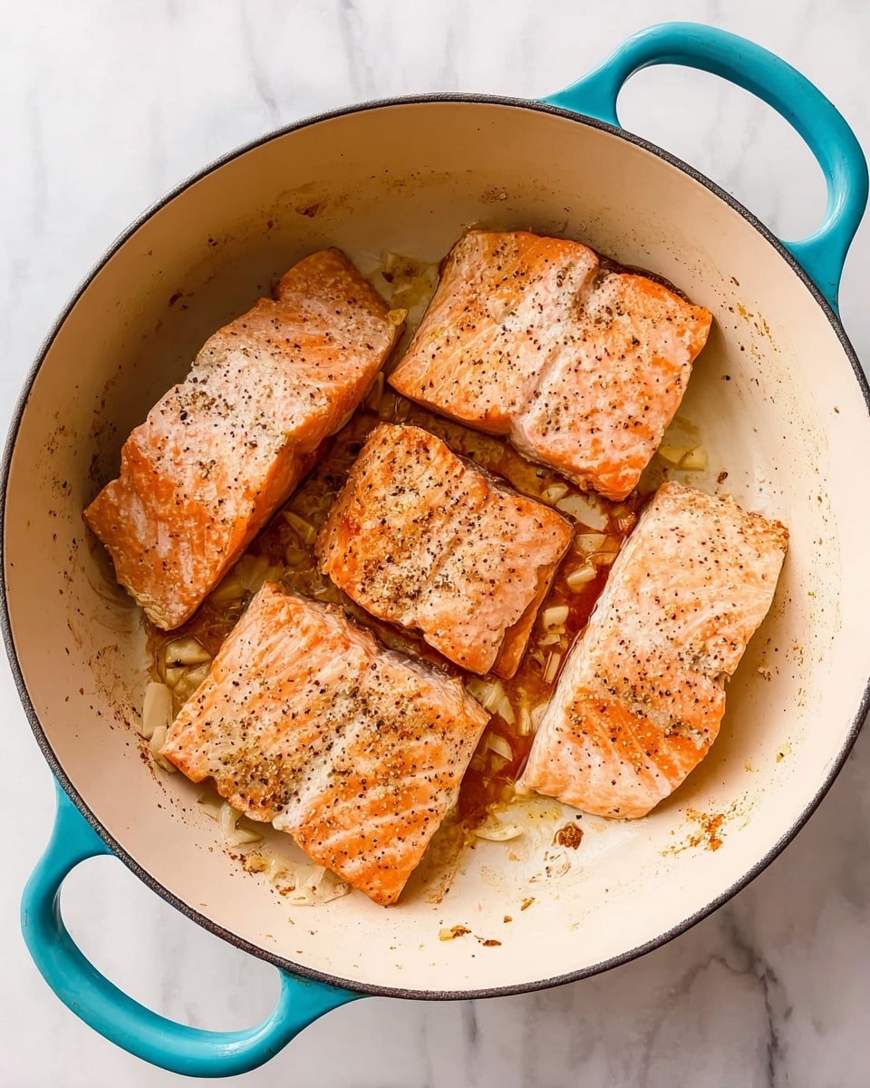 Four pieces of cooked salmon with a light golden brown color and visible pepper seasoning lie flat inside a large white cooking pot with turquoise handles on both sides. The salmon pieces are placed close together, showing a soft texture with light grill marks and slightly crisp edges. There are small bits of cooked garlic or onions around the fish, and the inner surface of the pot has slight browning stains from cooking. The pot sits on a surface with a white marbled texture. photo taken with an iphone --ar 4:5 --v 7