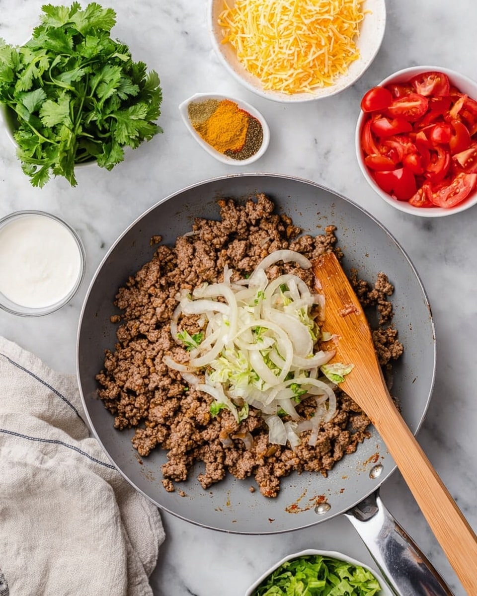 The image shows a gray frying pan filled with cooked ground meat topped with cooked sliced onions and various spices like yellow curry powder, black pepper, and red paprika in the center. A wooden spatula rests inside the pan on the food. Around the pan on a white marbled surface are small white bowls holding shredded yellow and white cheese, fresh green cilantro leaves, chopped green lettuce, and sliced red cherry tomatoes. A small white bowl with white sauce sits near the top left corner. A folded cloth napkin is partially visible at the bottom left. The whole setup is bright and colorful, with layers of ingredients ready to be combined photo taken with an iphone --ar 4:5 --v 7