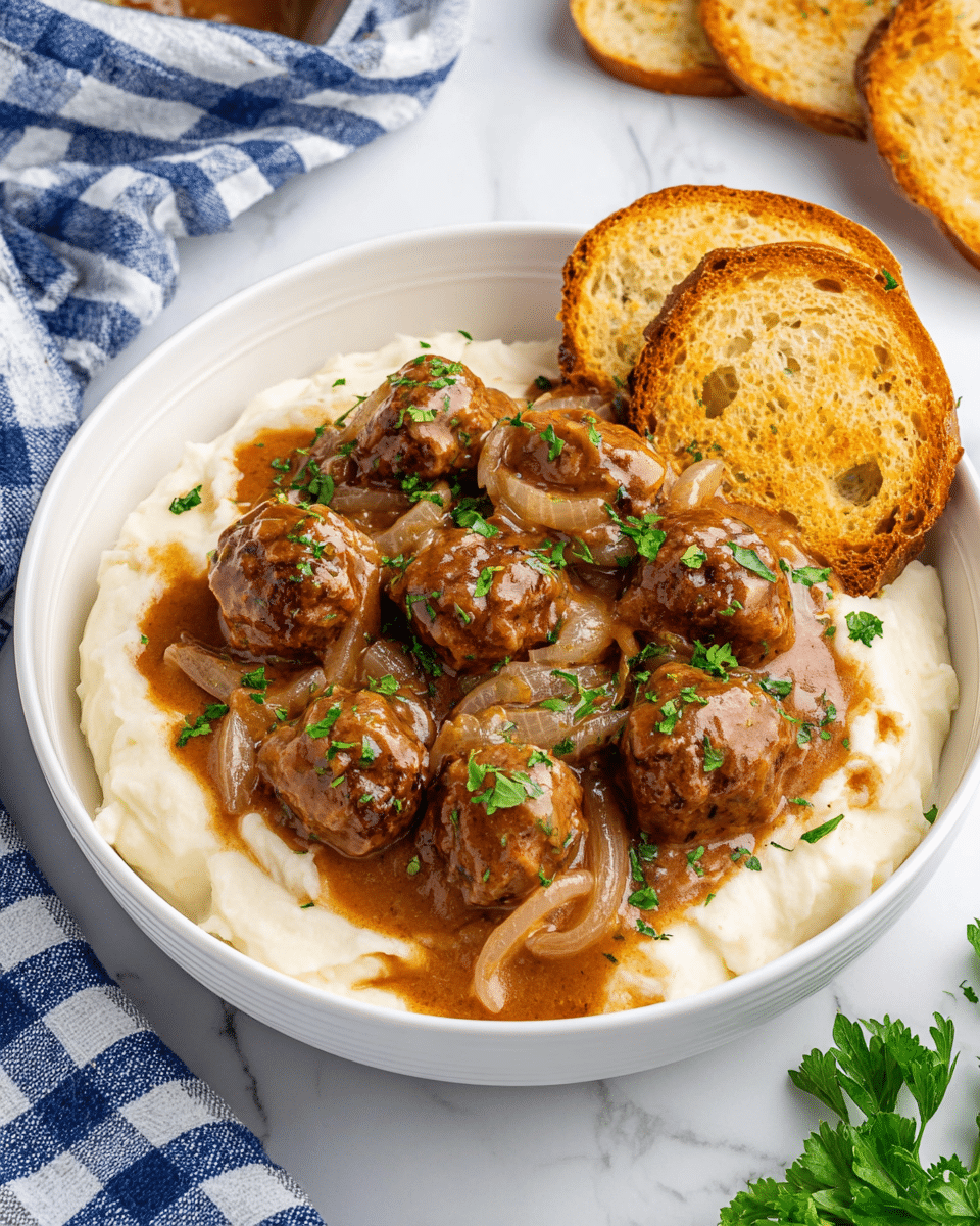 A white round bowl holds a base layer of creamy mashed potatoes, soft and fluffy with a smooth texture and slight lumps. On top, there is a thick layer of brown meatballs covered in a rich brown gravy mixed with sautéed translucent onion slices. The meatballs are garnished with small bright green parsley pieces scattered around. Two toasted slices of crusty bread, golden brown with visible air pockets and a crunchy texture, rest on the right side of the bowl. The bowl sits on a white marbled surface with some fresh parsley and a blue and white checkered cloth nearby. Photo taken with an iphone --ar 4:5 --v 7