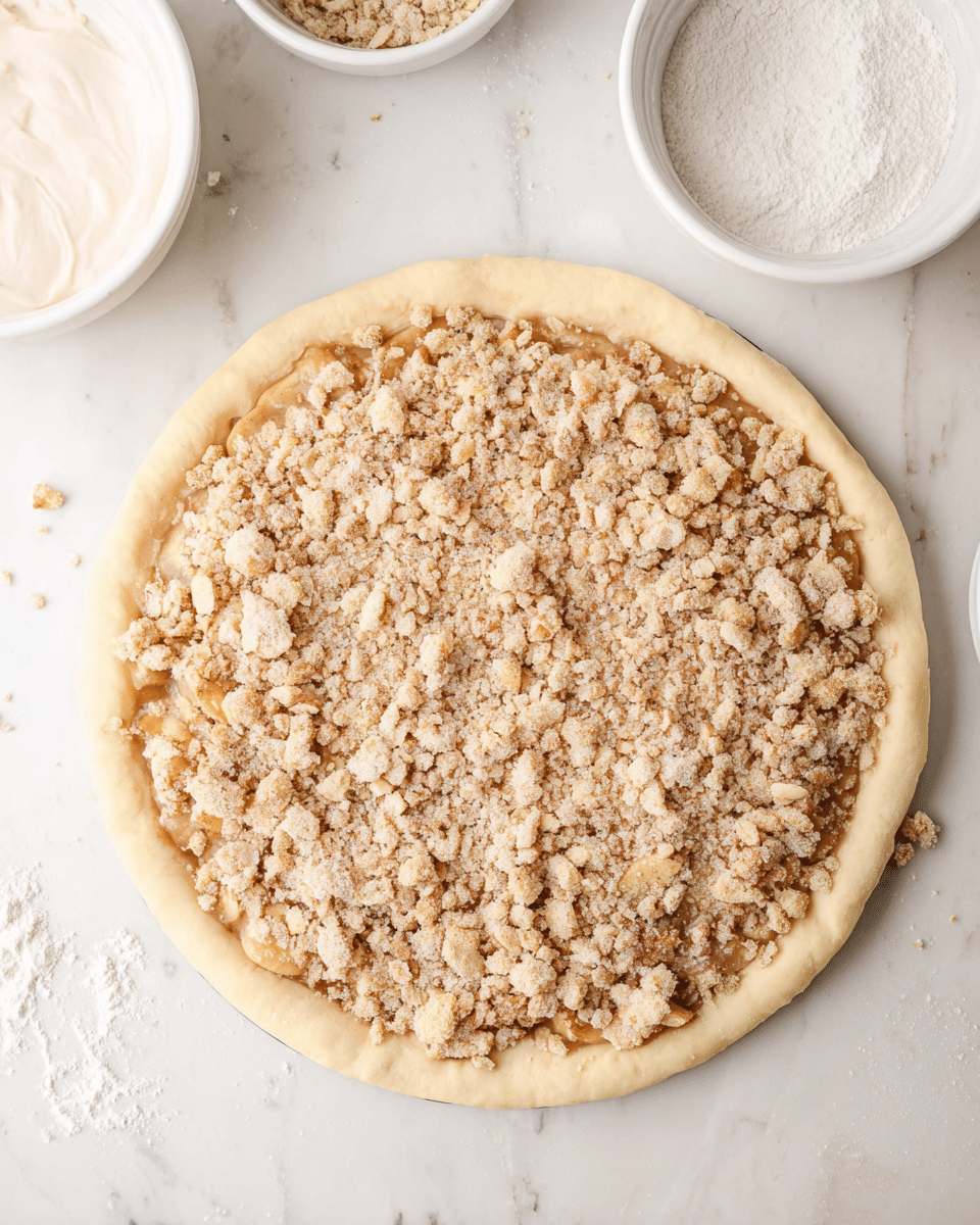 The image shows an uncooked pie placed on a white marbled surface, with a smooth, round crust forming the base layer. On top of the crust lies a thick layer of light brown filling, covered evenly with a crumbly topping made up of small and medium-sized beige chunks mixed with oat flakes. Around the pie, there are small white bowls, one empty with some cream residue and another with white powder, likely powdered sugar. The scene is bright and clean, emphasizing the textures of the crust and the crumbly topping. Photo taken with an iphone --ar 4:5 --v 7