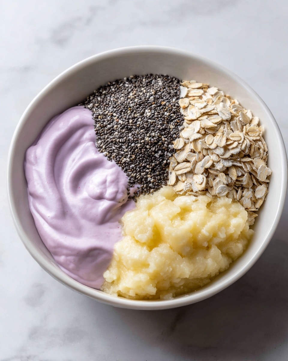 A close-up of a white bowl on a white marbled surface showing four distinct layers. The first layer is a smooth, light purple yogurt on the left. Next to it on the bottom left is a dense pile of small, black chia seeds. To the right of the chia seeds is a large heap of light beige rolled oats with a rough texture. The final layer on the top right is mashed banana, light yellow in color with a soft, chunky texture. The layers are arranged side by side, filling the bowl evenly. photo taken with an iphone --ar 4:5 --v 7