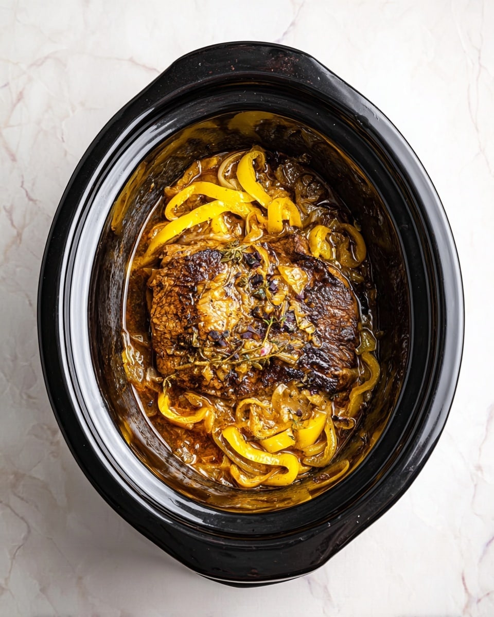 A black oval slow cooker filled with a cooked dish showing a large piece of browned meat in the center. The meat is topped and surrounded by soft cooked yellow pepper strips and translucent cooked onions in a brownish sauce. The surface beneath the slow cooker is a white marbled texture. photo taken with an iphone --ar 4:5 --v 7