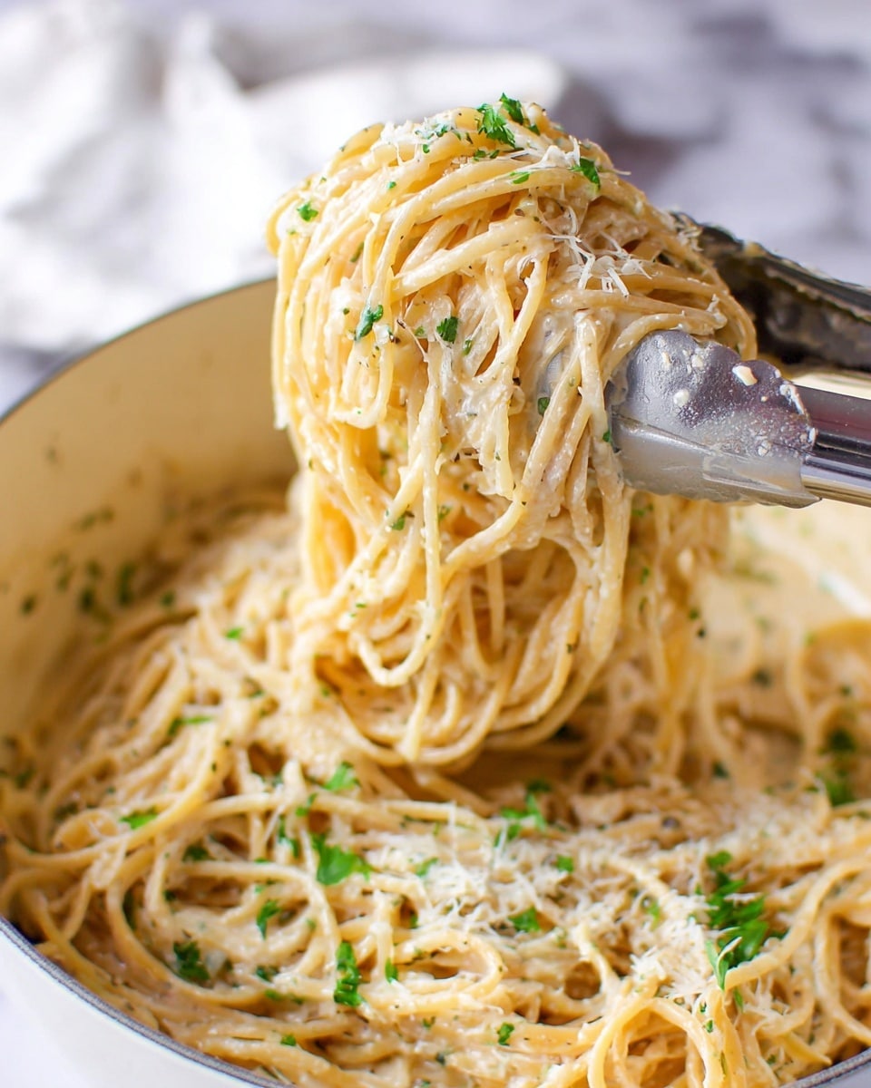 A bunch of long, thin spaghetti noodles covered in a creamy, light beige sauce is lifted with silver tongs above a white pot filled with the same pasta. The sauce looks smooth with small bits of herbs and grated cheese, giving some texture. Small green parsley leaves are scattered around the noodles adding bright green spots. The background shows a white marbled surface with a soft focus. Photo taken with an iphone --ar 4:5 --v 7