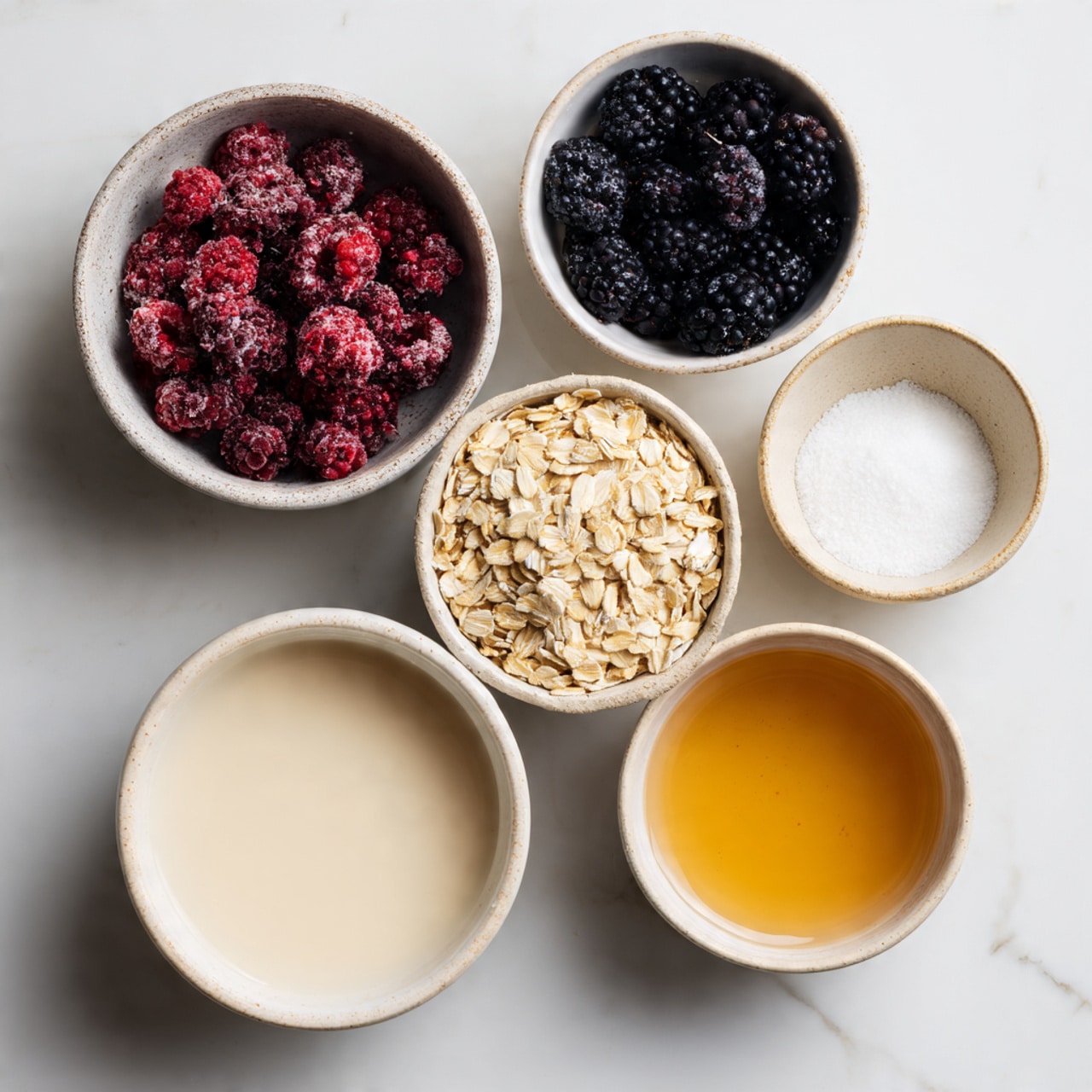 The image shows five small white bowls on a white marbled surface. The top left bowl contains frozen berries in shades of red, dark purple, and black, with a frosty texture. Below it is a bowl filled with light tan rolled oats, dry and flat. To the right of the oats is a bowl with white salt, fine and grainy. Above the salt is a bowl filled with light beige plant-based milk, smooth and creamy in texture. At the top right is a bowl with maple syrup, which is light golden and liquid. Each bowl is clearly labeled. Photo taken with an iphone --ar 4:5 --v 7