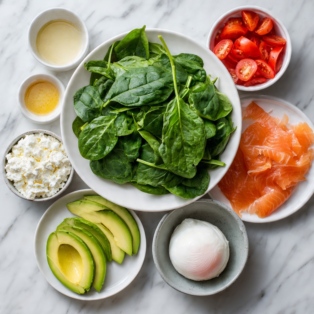 A large white plate filled with fresh spinach leaves, bright green and slightly glossy, arranged loosely across the surface. Around the main plate, smaller white bowls contain thinly sliced red tomatoes, bright and juicy; thin slices of orange-pink smoked salmon; a small white bowl with creamy white cottage cheese; a gray small bowl holding a perfectly poached egg with a soft white exterior and a hint of the pink yolk inside; and a small white bowl with a golden yellow dressing or sauce. A separate small white plate holds thin, even slices of ripe avocado with a vibrant green color, neatly fanned out. All dishes sit on a white marbled surface, creating a fresh and clean look. photo taken with an iphone --ar 4:5 --v 7