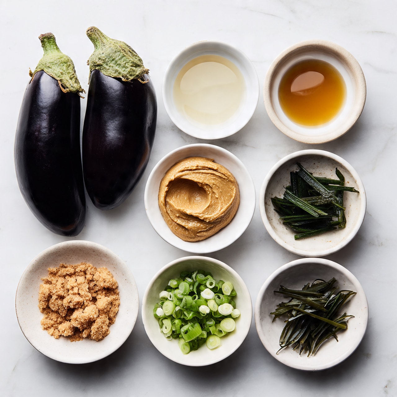 Two whole dark purple eggplants sit side by side at the top of the image on a white marbled surface. Below them are three small white bowls in a row: the left bowl holds a clear, slightly oily liquid; the middle bowl has a thick tan paste with a smooth texture; the right bowl contains a clear, watery liquid. In front of these are another three small white bowls: the left one filled with soft brown sugar clumps; the middle one with chopped light and dark green scallions; and the right one with thin, dark green strips of seaweed. The overall layout is neat and organized, showing fresh and varied ingredients. photo taken with an iphone --ar 4:5 --v 7