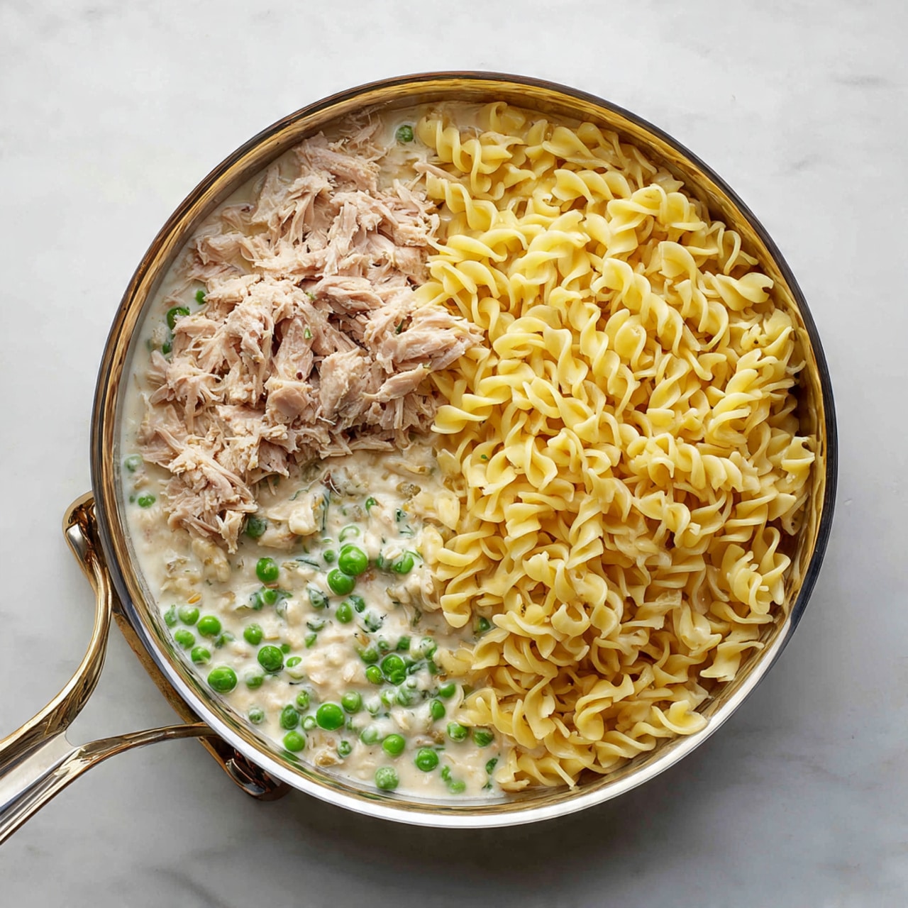 A white marbled surface holds several ingredients arranged neatly in small clear glass bowls and containers. At the center top is a large white bowl filled with uncooked curly egg noodles in a pale yellow color. To its right is a clear plastic package with whole white mushrooms. Below the noodles, there are two small glass bowls: one with bright green peas and the other with light brown breadcrumbs. To the left, a small glass bowl contains white flour, and next to it is a medium-sized yellow onion. Above the onion, a small clear bowl holds salt and black pepper. Nearby, a round can of chunk light tuna in water has a blue label, and next to it is a small stick of butter with markings. Above the butter, a small bowl of grated Parmesan cheese sits close to a bowl of cream cheese. On the left side, a small glass pitcher contains white milk, and next to it, a small glass bowl holds light yellow chicken broth. The whole scene is bright and clean with a white marbled texture under everything. photo taken with an iphone --ar 4:5 --v 7