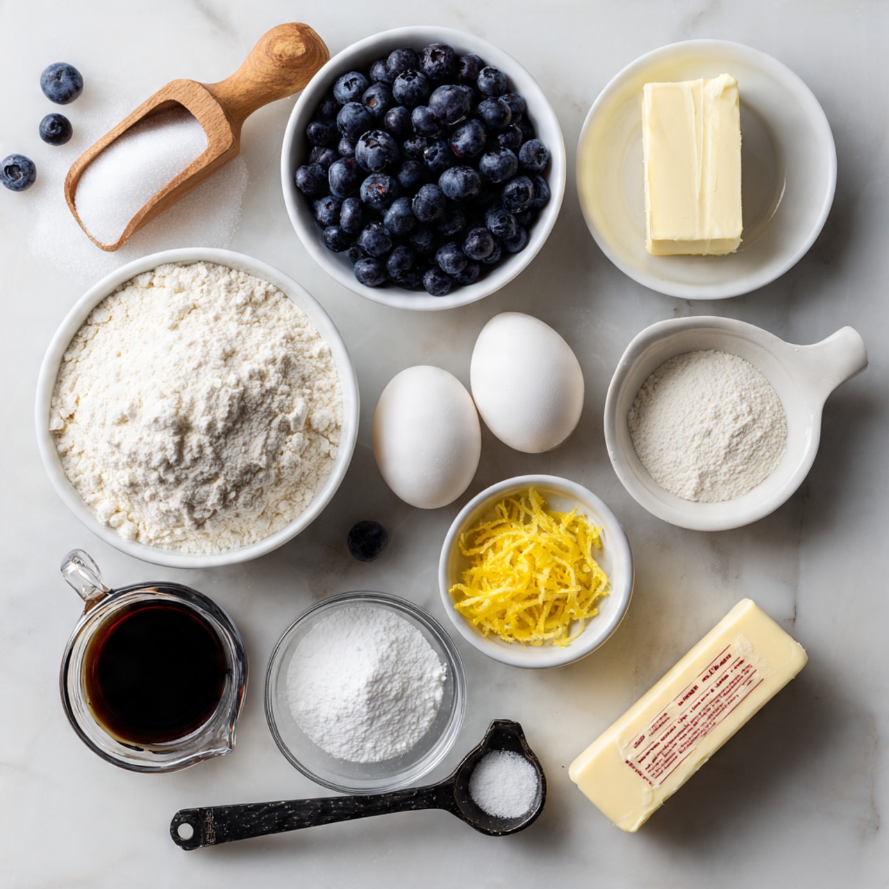 A flat lay of baking ingredients on a white marbled surface, showing nine main items arranged neatly. At the top left, a wooden scoop filled with white sugar sits next to a white bowl loaded with fresh dark blueberries, with a few scattered blueberries nearby. Below the sugar, a white bowl holds a rectangular block of cream cheese, while two white eggs rest side by side nearby. Centered is a white bowl heaped with white flour. To the right, a small white bowl contains three small piles of white powders (likely baking soda, baking powder, and salt), next to a small dark spoon-shaped bowl filled with bright yellow lemon zest. Below the zest, a small clear measuring cup has a dark liquid, probably vanilla extract. On the bottom left, a clear measuring cup contains a creamy white liquid, and at the bottom right lies a stick of butter with faded red lettering. Photo taken with an iphone --ar 4:5 --v 7