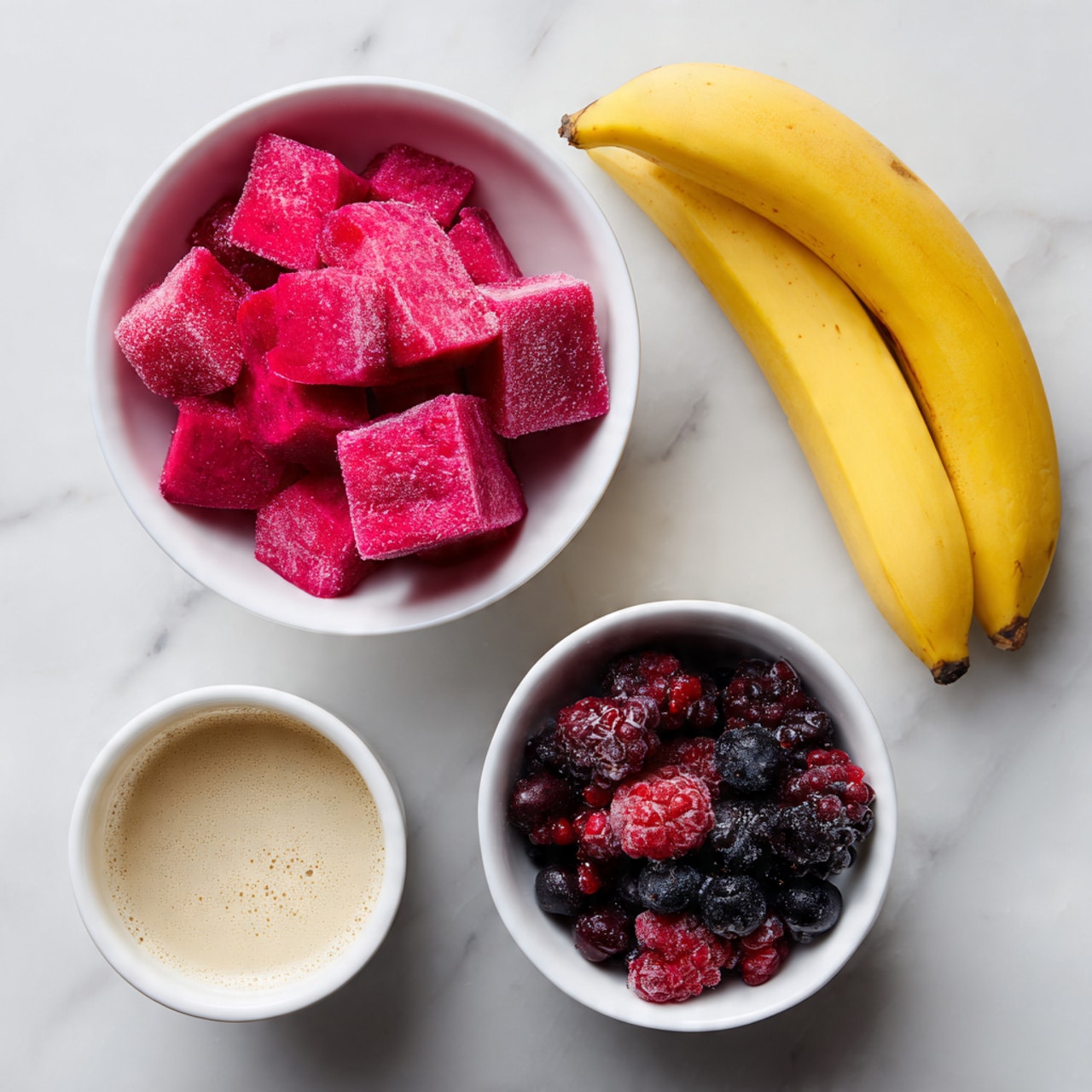 The image shows four main items placed on a white marbled surface. At the top left, there is a white bowl filled with bright pink frozen pitaya cubes, showing a rough, icy texture. To the right of the bowl, a whole yellow banana with slight brown spots rests with its curved shape clear and smooth. Below the banana, at the bottom right, another white bowl contains mixed frozen berries in deep red, purple, and black colors with frosty surfaces. At the bottom left, a small white cup holds a light beige liquid labeled as coconut water, with small bubbles on its surface. The items are neatly arranged with labels beside each one. Photo taken with an iphone --ar 4:5 --v 7