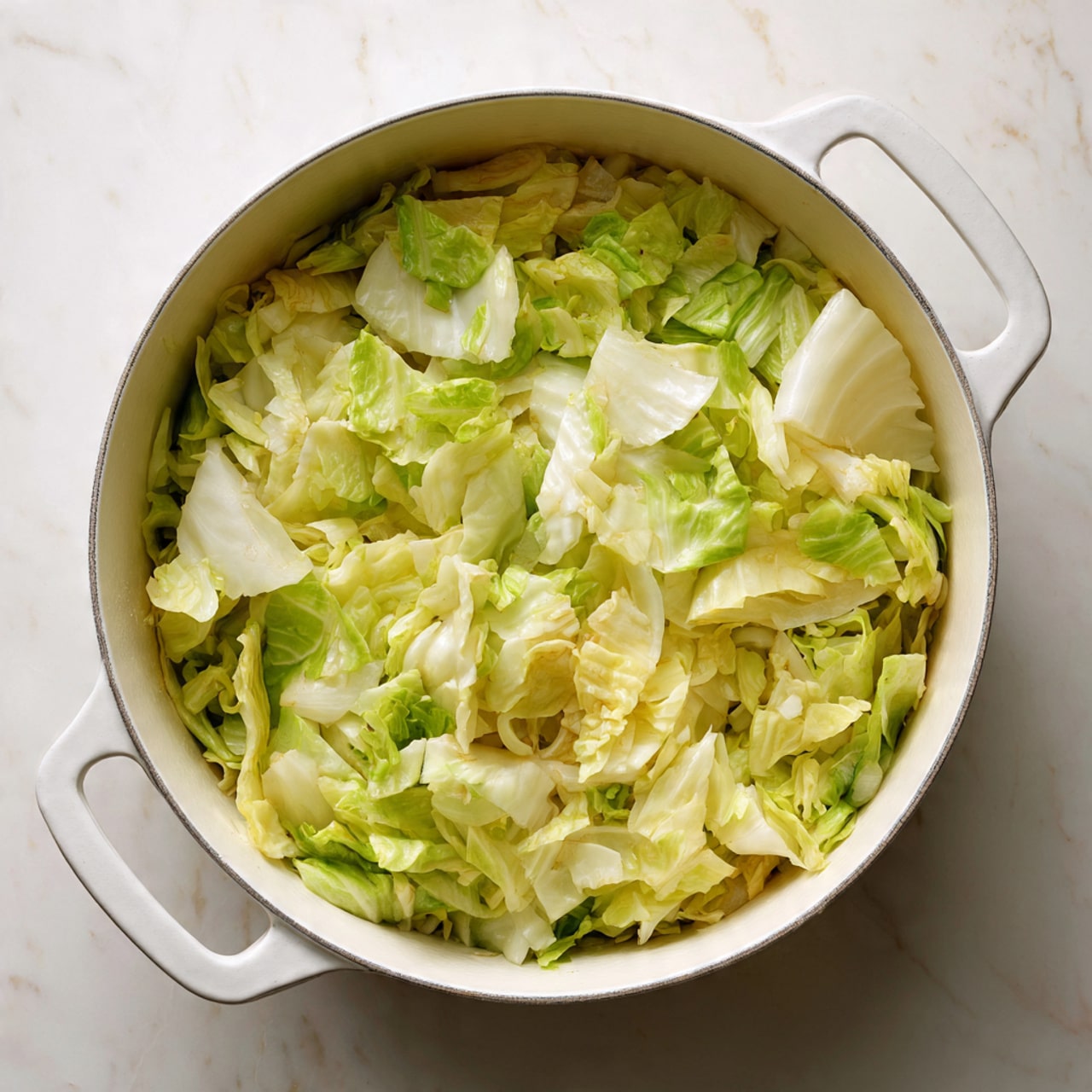A white pot with two handles is filled with chopped cabbage arranged in one thick layer, showing a mix of light green and pale yellow leaves with some crinkled and others smooth textures. The cabbage pieces are unevenly spread, revealing some small bits of onion underneath, with the pot placed on a white marbled surface. photo taken with an iphone --ar 4:5 --v 7