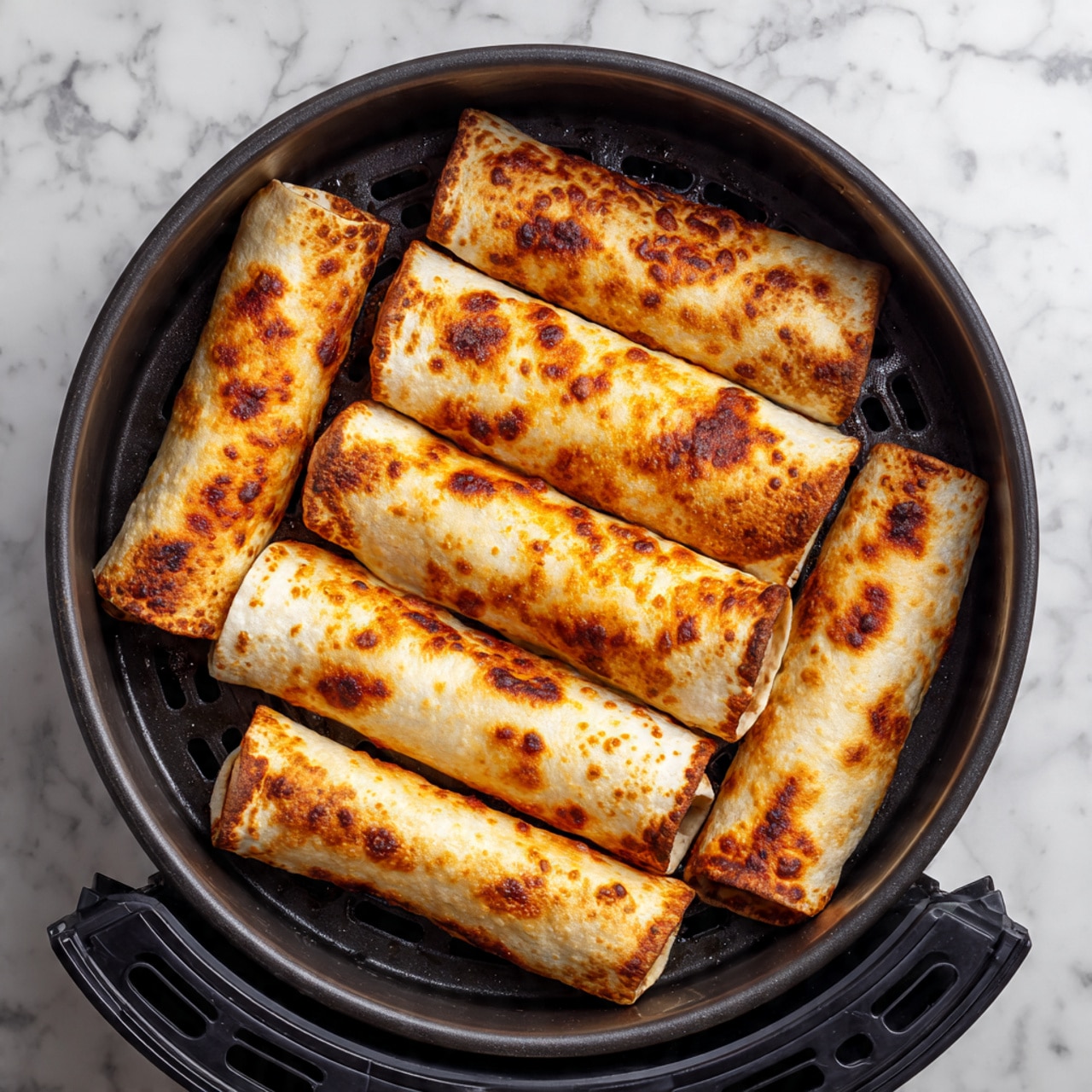 The image shows nine golden brown, crispy triangular pockets arranged in a black air fryer basket with a perforated base. Each pocket has browned edges and spots where the surface turns a darker amber, showing a well-cooked, slightly textured dough that looks crunchy. The pockets are spread evenly with small gaps in between, and the air fryer basket has a matte black finish with geometric cutouts visible underneath. The overall tone highlights warm golden colors and textures against the deep black basket and white marbled surface below. photo taken with an iphone --ar 4:5 --v 7