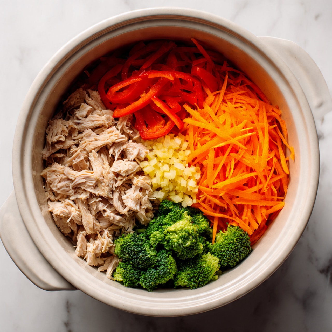 A white pot filled with four main layers of ingredients arranged in separate sections: at the bottom layer are small pieces of light tan cooked chicken spread across the pot, on the left side above the chicken are thin, bright red strips of bell pepper, on the bottom right side there is a pile of shredded bright orange carrots, and on the top right are several small, fresh green broccoli florets with a small pile of finely minced garlic next to them. The pot is placed on a white marbled surface. Photo taken with an iphone --ar 4:5 --v 7