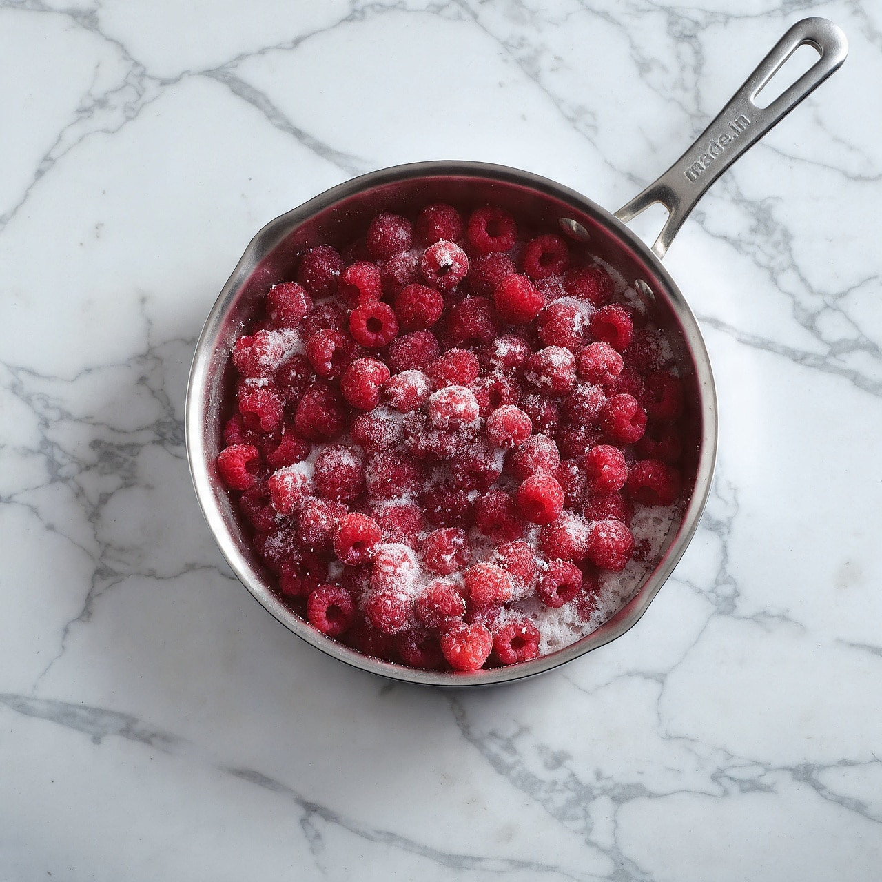A close-up view inside a metal mixing bowl where a creamy white mixture with light, fluffy texture sits at the bottom. On top of the creamy layer, there are splashes and small pools of dark red liquid sauce, creating a contrast between the white and dark red. The metal mixing equipment is slightly visible at the top part of the image. The bowl is placed on a white marbled surface. photo taken with an iphone --ar 4:5 --v 7