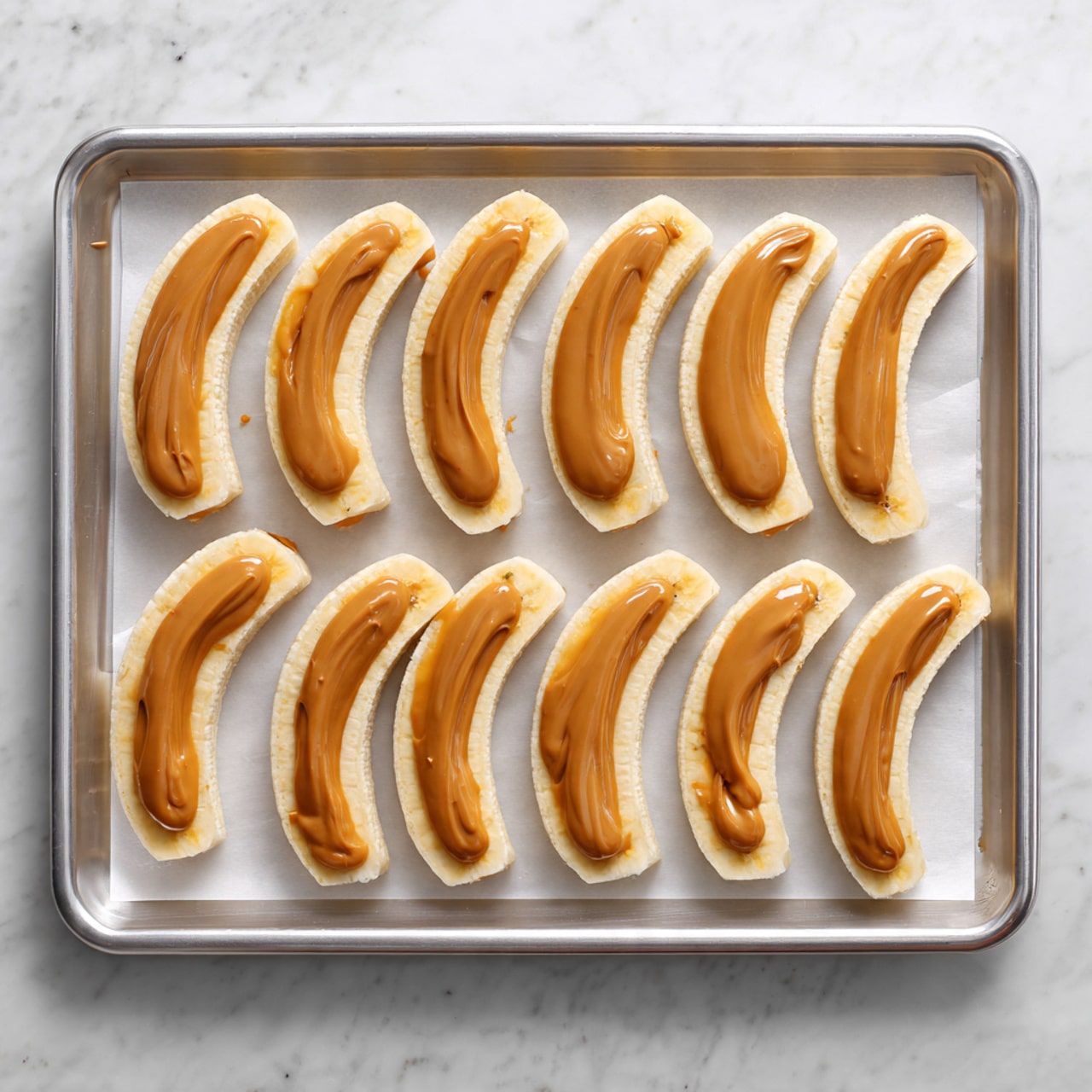 The image shows a metal baking tray with a layer of white parchment paper on top, placed on a white marbled surface. On the tray, there are ten evenly spaced small, crescent-shaped pastries arranged in two rows. Each pastry is golden brown and topped with small bits of white nuts or crumbs, giving a lightly textured look. The pastries have a smooth, lightly shiny surface with some small cracks and a slightly curved shape. Photo taken with an iphone --ar 4:5 --v 7