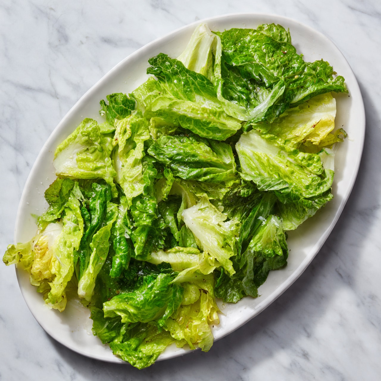 An oval white plate is filled with a single layer of fresh lettuce leaves. The lettuce is mixed with light green and dark green pieces, showing a variety of textures from soft, light green leaves to crisp, dark green ones. The plate sits on a white marbled surface and the lettuce looks fresh and bright. photo taken with an iphone --ar 4:5 --v 7