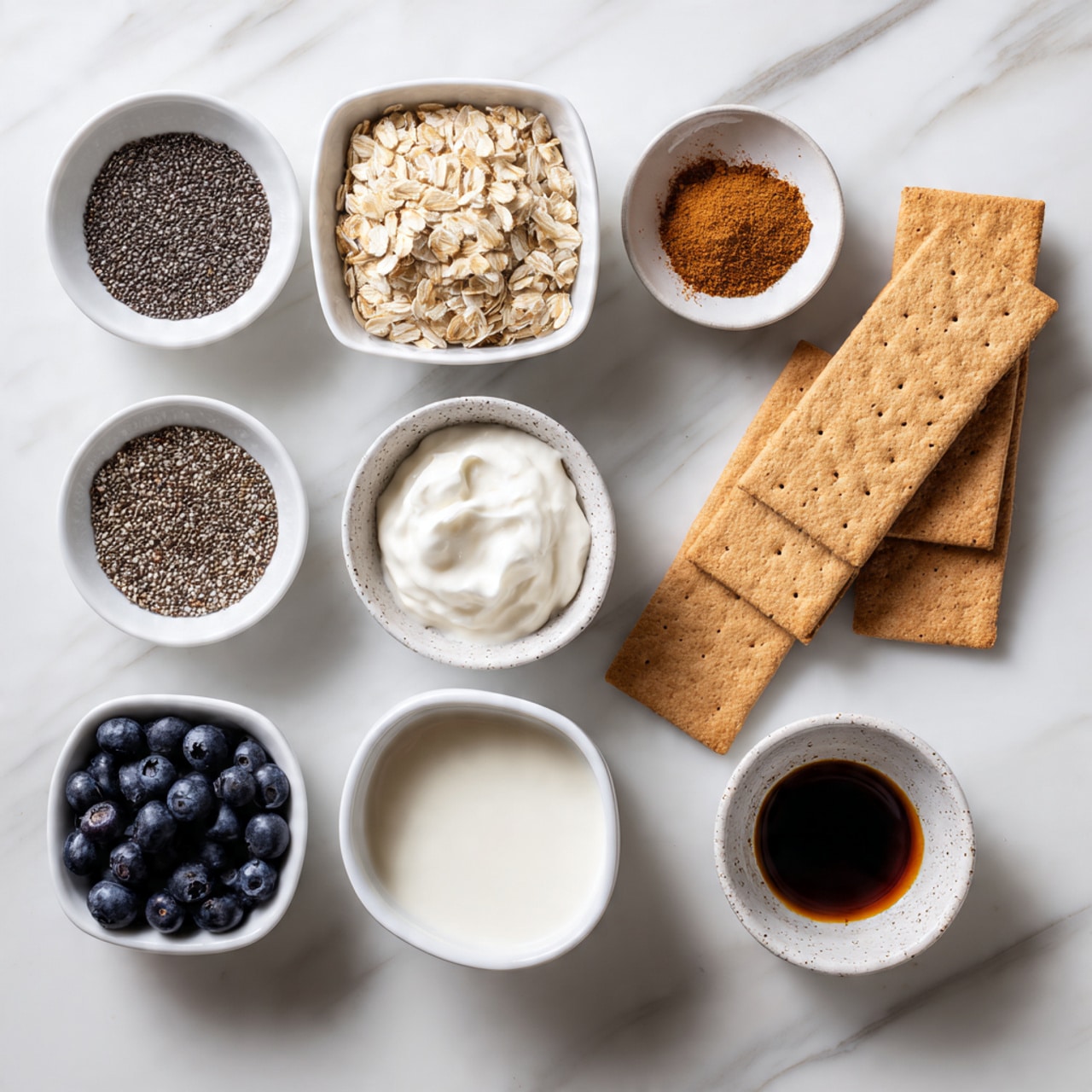 The image shows nine small white bowls and two white rectangular graham crackers arranged neatly on a white marbled surface. Each bowl contains one ingredient: dark small chia seeds, light beige rolled oats, white creamy Greek yogurt, dark brown cinnamon powder, dark brown maple syrup, dark blue blueberries, white almond milk in a speckled bowl, and dark vanilla extract in a small bowl. The two rectangular graham crackers are positioned near the top right corner, with slight overlapping. Each ingredient is clearly visible with a clean and simple presentation, labeled with white text boxes above or beside each element. Photo taken with an iphone --ar 4:5 --v 7