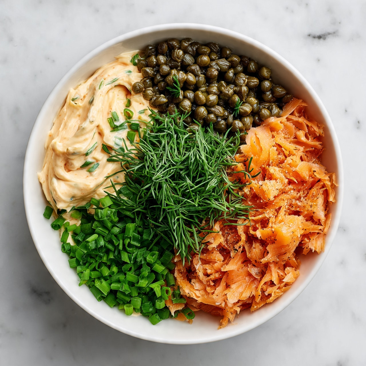 A white bowl filled with a creamy white dip that has small green and orange bits mixed in, giving it a textured look; on top, there are three thin slices of pinkish smoked salmon arranged slightly overlapping in the center, sprinkled with fresh chopped green herbs and scattered dark green capers; a silver spoon is placed inside the bowl, partially submerged in the dip at the bottom right. Around the bowl, plain round golden crackers are placed neatly along the edge of the bowl. Everything is set on a white marbled surface with a striped cloth partially visible at the bottom left photo taken with an iphone --ar 4:5 --v 7
