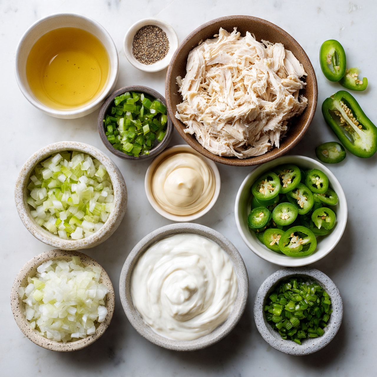 The image shows an overhead view of various ingredients arranged neatly on a white marbled surface. At the center bottom, there is a white bowl filled with pale shredded chicken. Above this bowl, a brown bowl holds white Greek yogurt with a smooth, creamy texture. To the right of the yogurt, a small white bowl contains chopped green jalapeños with a fresh and moist look. Below the jalapeños, a slightly larger brown bowl is filled with finely chopped white sweet onion. To the left of the onion, a small white bowl holds clear yellow jalapeño brine with a smooth surface. Next to the brine bowl, a small stone-like container holds a dollop of pale mayonnaise with a shiny finish. Above the mayo, a grey bowl is filled with green chopped celery, displaying a crisp texture. To the left of the celery, a white bowl contains a mix of spices: black pepper, salt, and a beige powder. On the bottom right corner, a small white bowl holds finely chopped dark green pickled jalapeños. Several slices of fresh jalapeño peppers, bright green with seeds visible, are placed around the bowls. The overall setting has a clean and organized look. Photo taken with an iphone --ar 4:5 --v 7