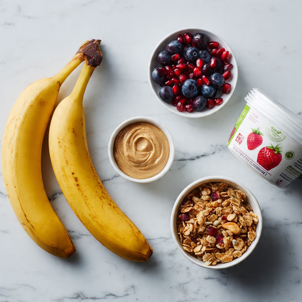 A white plate holds a split banana placed in the center with two halves curved inward, creating a small boat shape. Inside the banana boat, there is a layer of creamy white yogurt with a smooth texture. On top of the yogurt, there is a scattering of golden granola clusters, bright red pomegranate seeds, and plump dark blue blueberries that add pops of color and texture. Some granola and fruit pieces spill slightly onto the plate around the banana. The plate is set on a surface with a white marbled texture. photo taken with an iphone --ar 4:5 --v 7