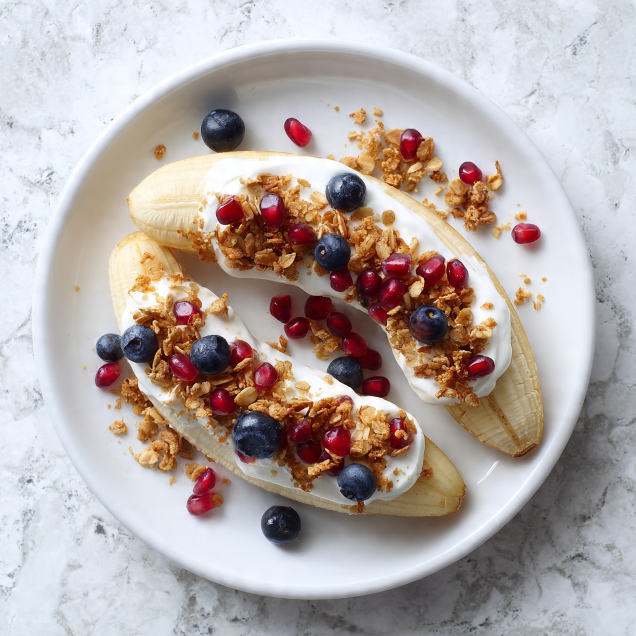 A peeled banana is laid flat on a white plate with a layer of white creamy yogurt in the middle. On top of the yogurt, there is a scatter of small clusters of light brown granola, bright red pomegranate seeds, and plump dark blue blueberries. Smooth light brown almond butter is drizzled over the fruit and granola, adding a textured swirl across the plate. A golden fork rests on the right edge of the plate. The plate sits on a white marbled surface photo taken with an iphone --ar 4:5 --v 7