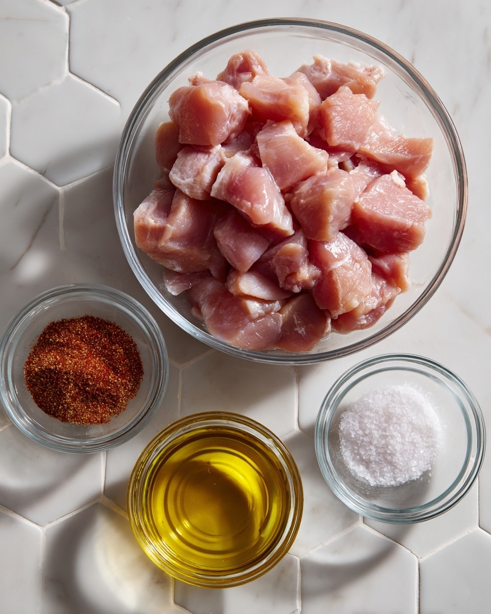 A clear glass bowl in the center holds many pieces of light pink raw chicken chunks with a smooth texture. Below this bowl are three smaller clear glass bowls arranged in a slight curve: the left one contains a reddish-brown taco seasoning, the middle one has bright golden olive oil, and the right one holds white salt crystals. All the bowls sit on a white marbled hexagonal tile surface. The photo is taken with an iphone --ar 4:5 --v 7