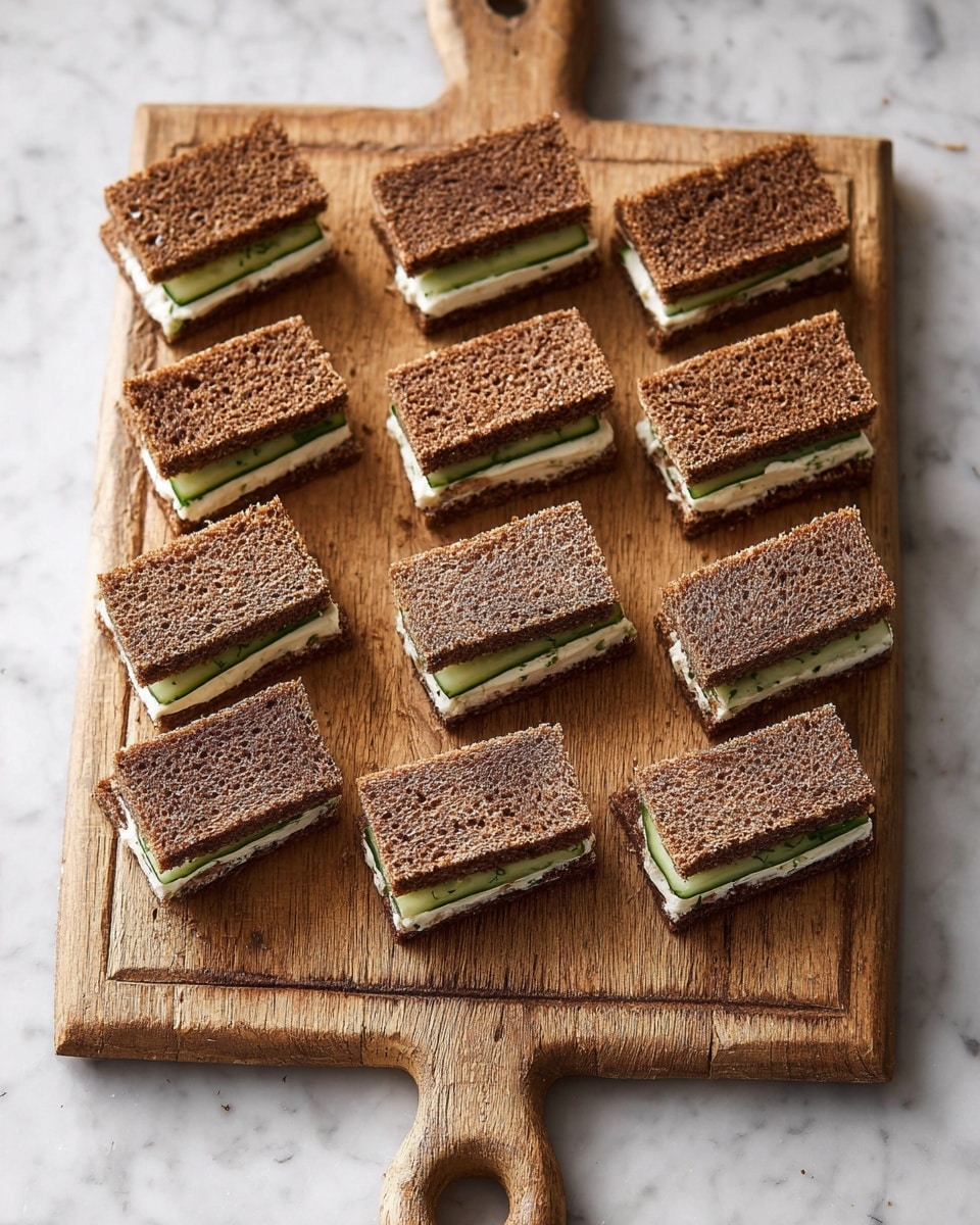 There are twelve small rectangular sandwiches arranged on a wooden cutting board with a handle. Each sandwich has three layers: dark brown bread on the top and bottom, and a light creamy filling with thin green cucumber slices in the middle layer. The texture of the bread is dense and grainy, while the filling is smooth. The cutting board is placed on a white marbled surface. photo taken with an iphone --ar 4:5 --v 7