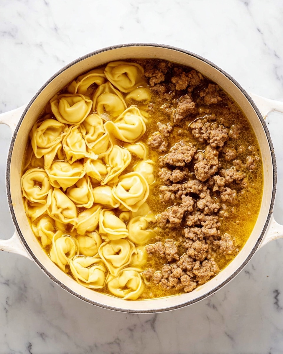 Inside a large white pot, there are two main layers clearly divided: one side shows yellow tortellini pasta floating in golden broth with a smooth, slightly shiny texture, while the other side contains browned ground meat in small chunks, also sitting in broth with a slightly oily surface. The pot sits on a white marbled surface, and the rich color contrast between the yellow pasta and brown meat in the light broth is visually striking. photo taken with an iphone --ar 4:5 --v 7