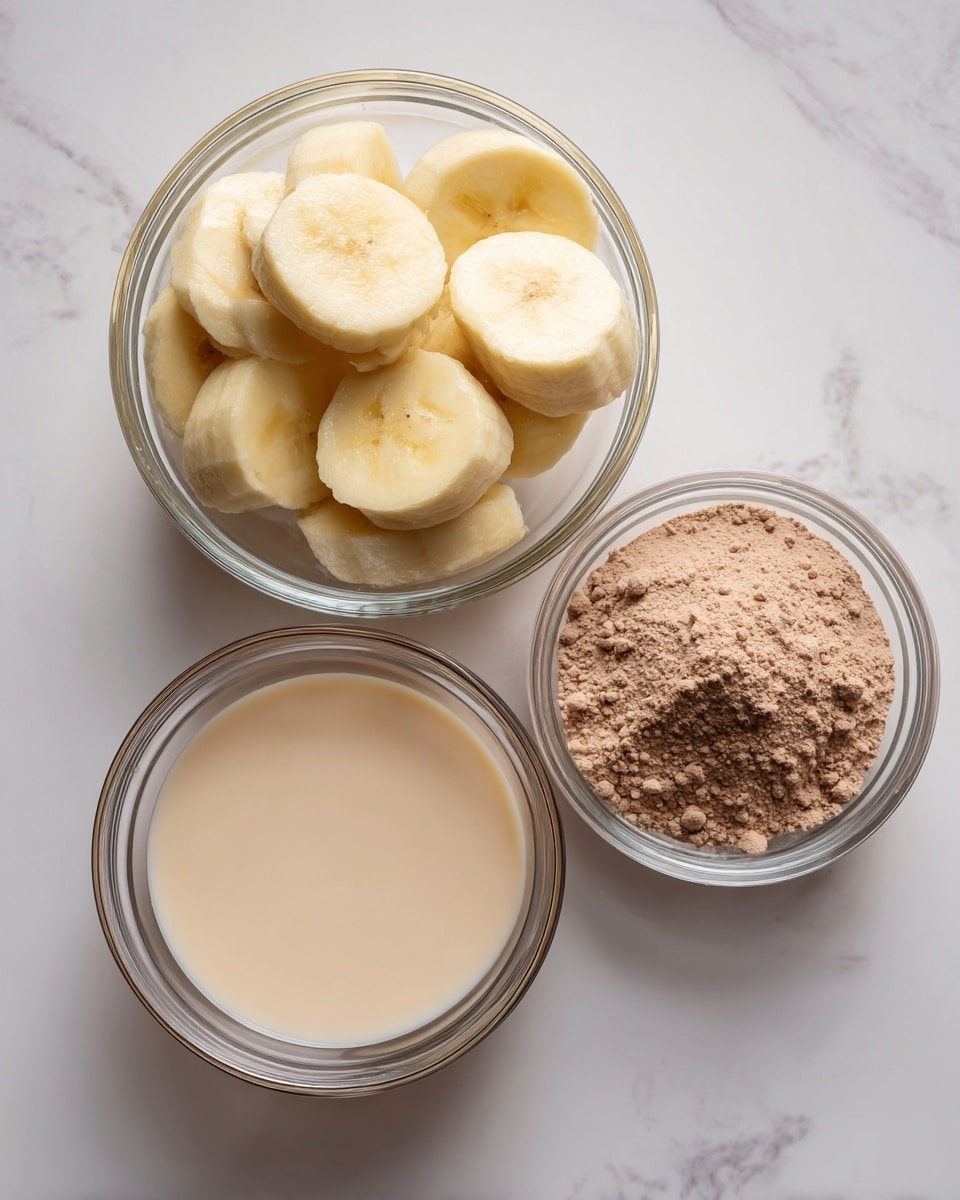 Three clear glass bowls are arranged on a white marbled surface. The largest bowl at the top left is filled with thick, round slices of pale yellow frozen bananas. To the right of it, a smaller bowl contains a fine, light brown powder labeled as chocolate protein powder. Below these two bowls is another small bowl filled with a smooth, creamy pale beige liquid labeled milk. The bowls have a simple design with visible circular ridges. photo taken with an iphone --ar 4:5 --v 7