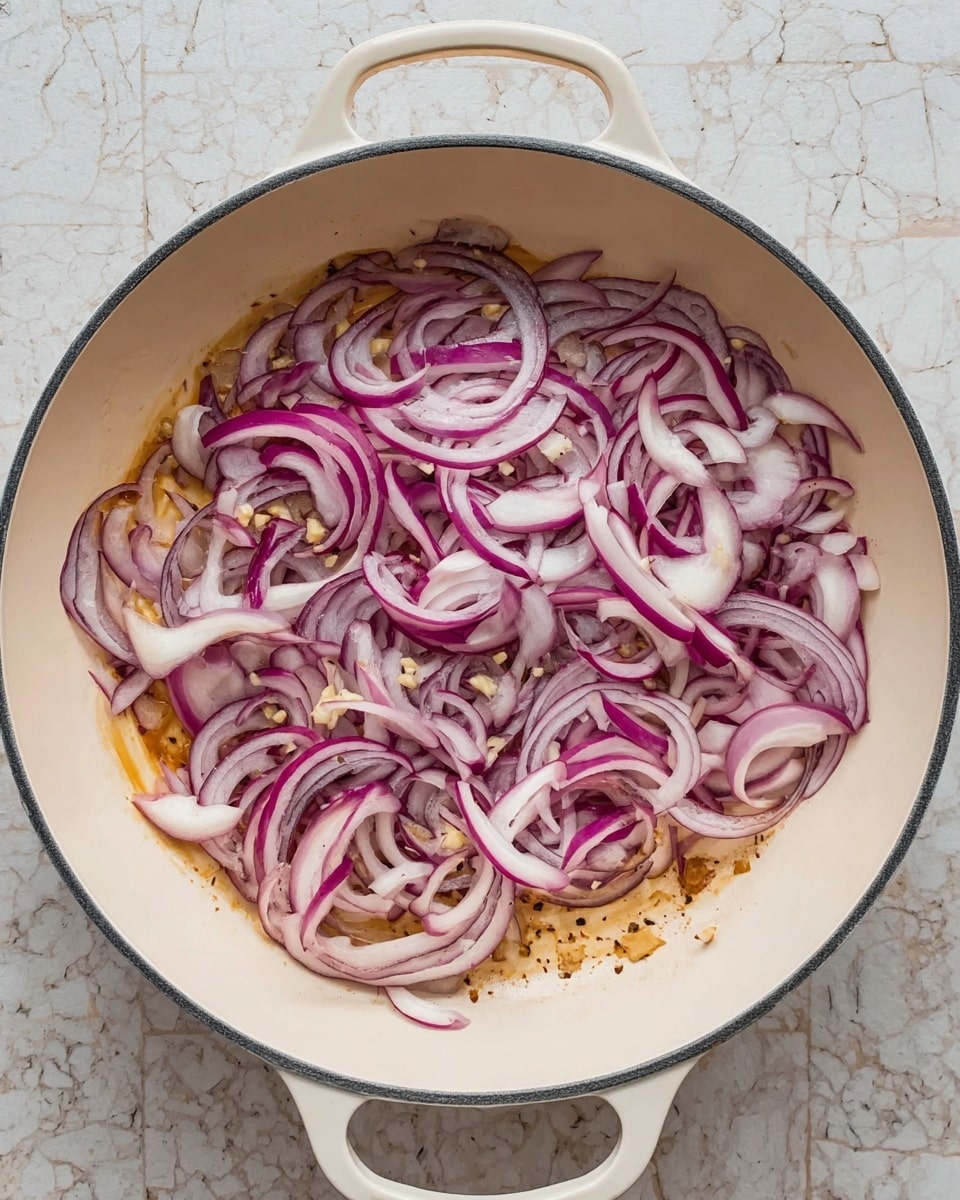 A white pan with two handles contains thinly sliced red onions and small pieces of chopped garlic spread evenly over the bottom. The onions show a mix of purple and white colors with some parts slightly translucent, indicating they are being cooked. The pan base shows a light golden brown texture from cooking, and the scene is set on a white marbled surface. photo taken with an iphone --ar 4:5 --v 7