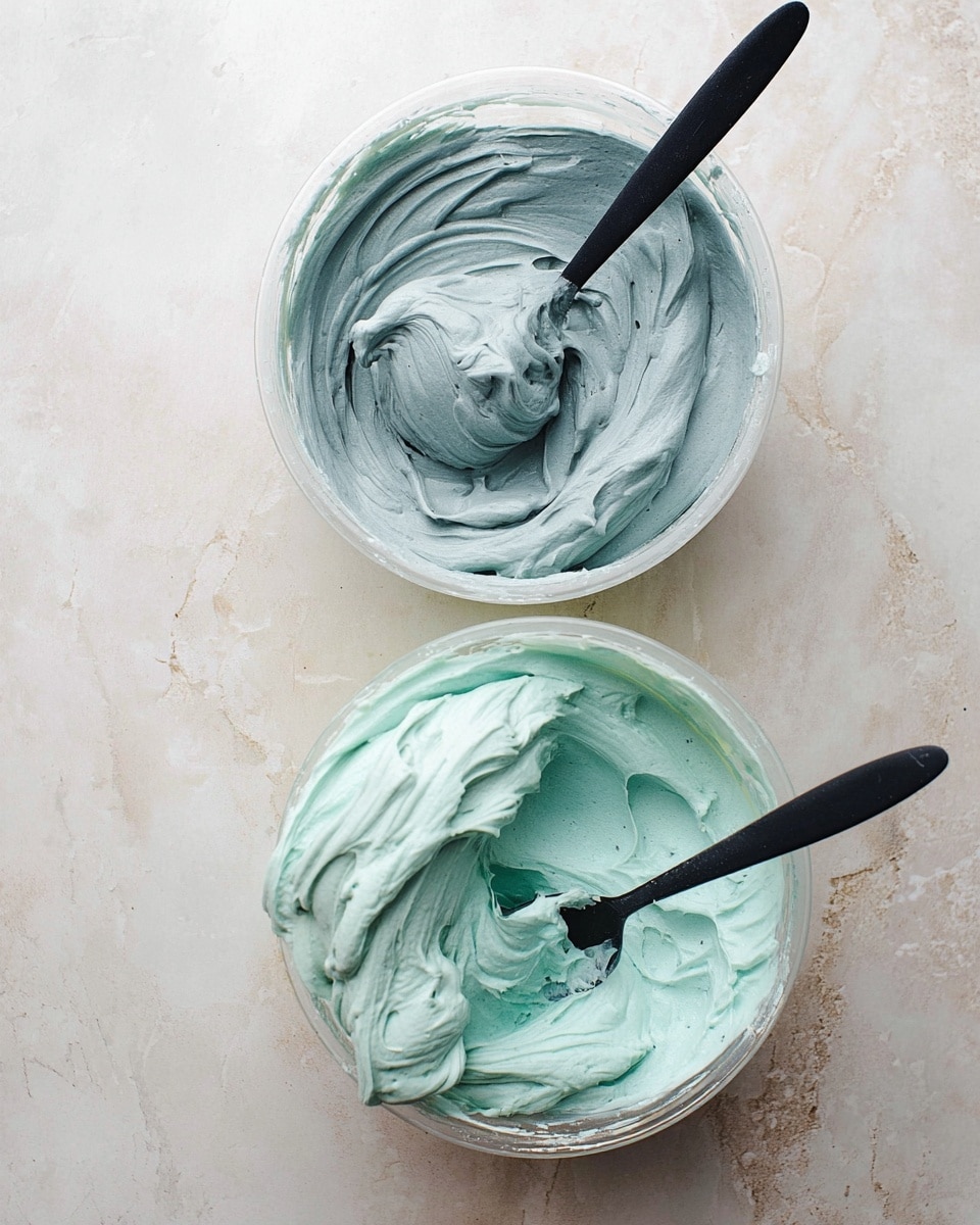 Two clear bowls sit on a white marbled texture surface, each filled with smooth, thick cream. The top bowl holds a grey-blue cream that is swirled with soft peaks, and a black spoon rests inside it, slightly covered by the cream. The bottom bowl contains a light turquoise cream with a similar texture, and a black spoon with some cream on its edge lies inside it. Both creams look fluffy and thick, with visible swirls and soft folds. Photo taken with an iphone --ar 4:5 --v 7